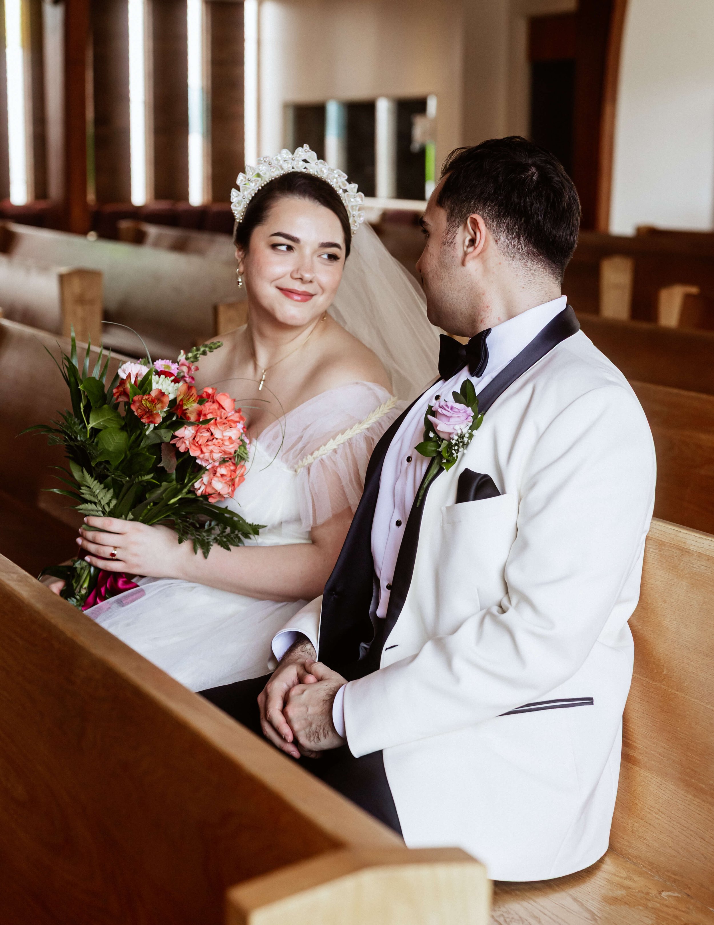 Un homme et une femmes sont assis sur des bancs d'église, une femme à un bouquet de fleur dans les mains. Ils se regardent.