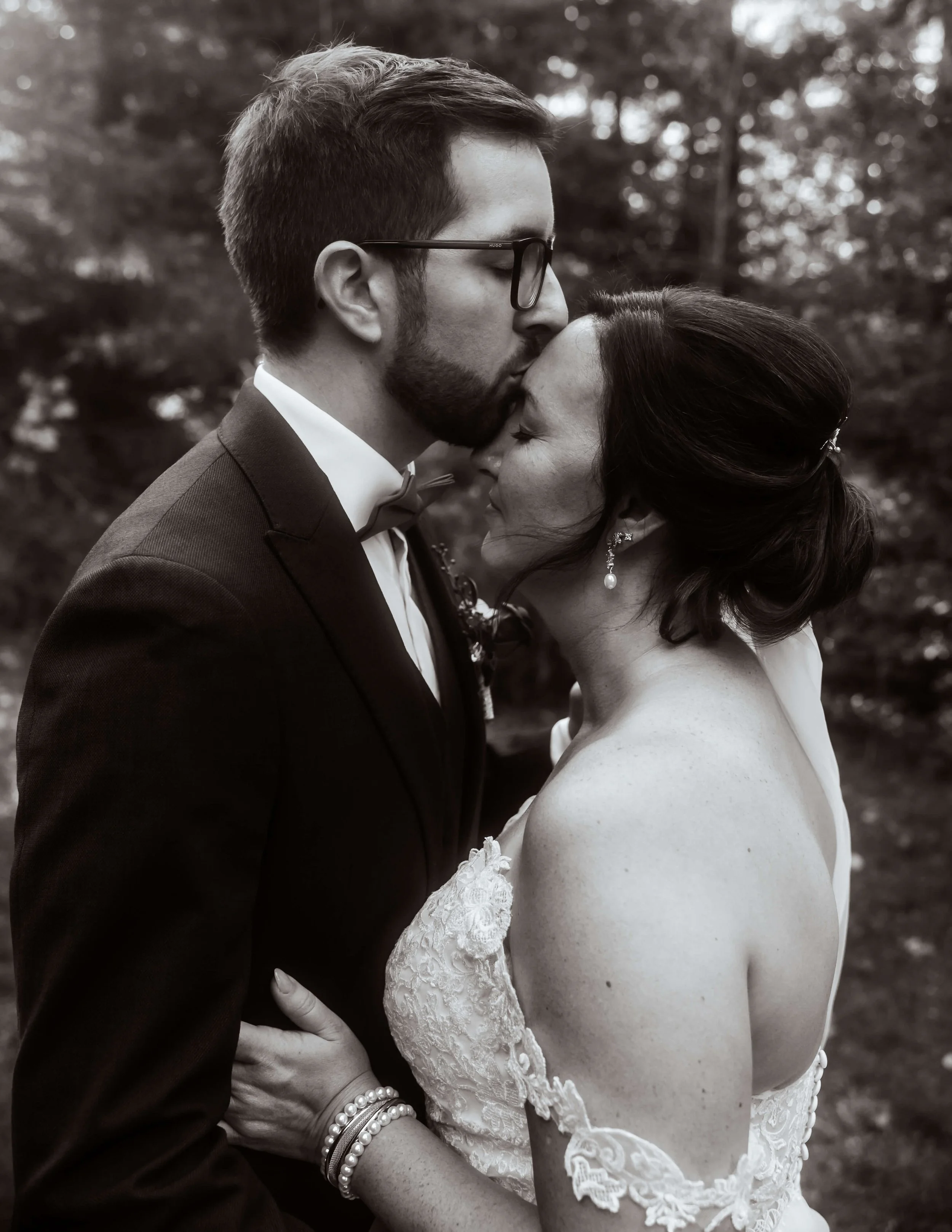 Un couple en costume de mariage partage un moment intime dans un parc montréalais, la femme ferme les yeux tandis que l'homme la serre et la console avec tendresse