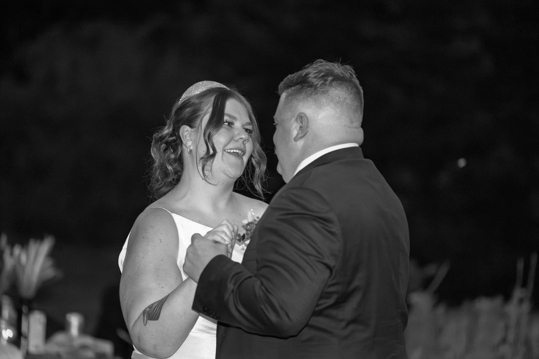 A couple sharing a dance at their wedding reception, smiling at each other.