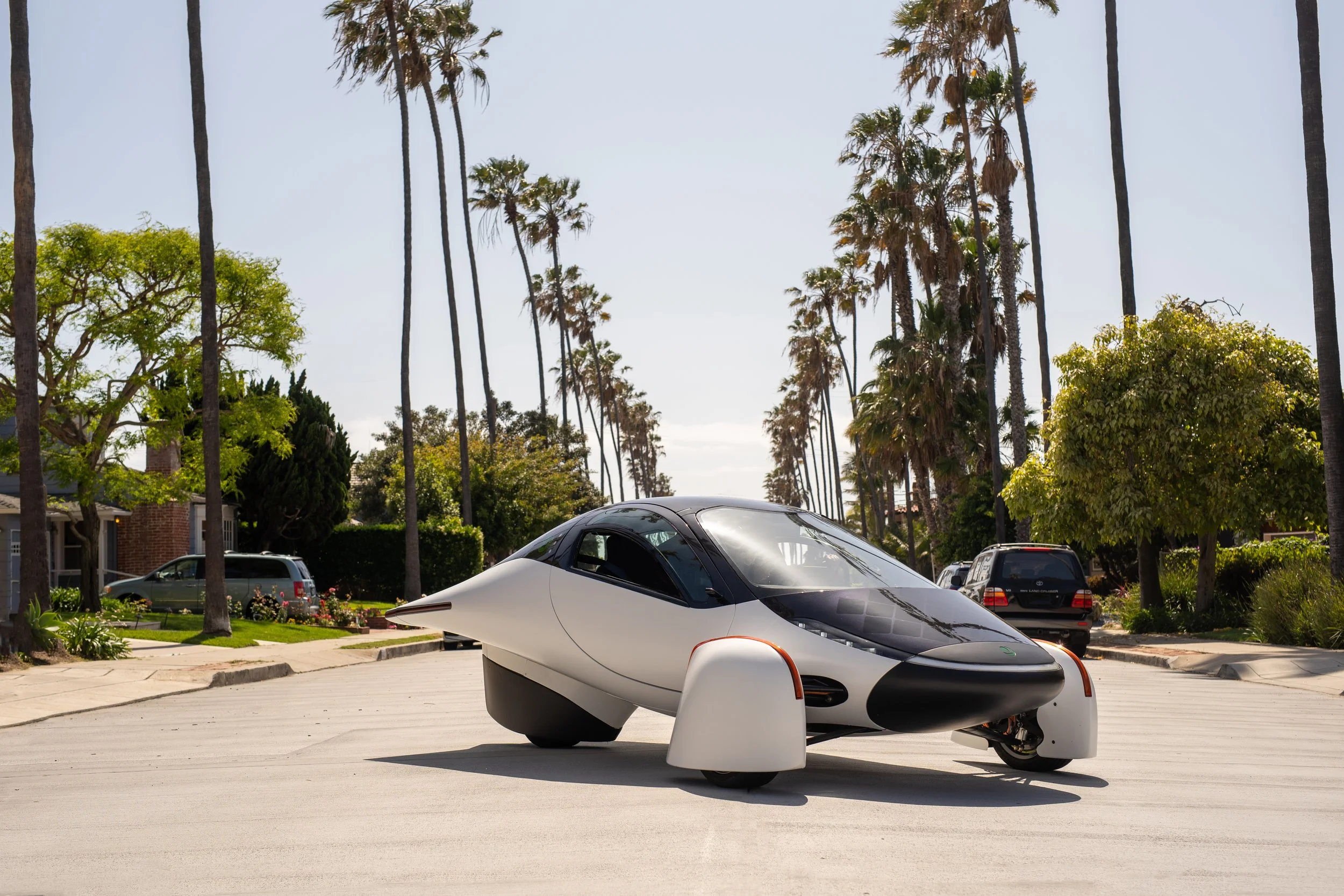 Aptera white vehicle parked in center of the road with palm trees lining the streets