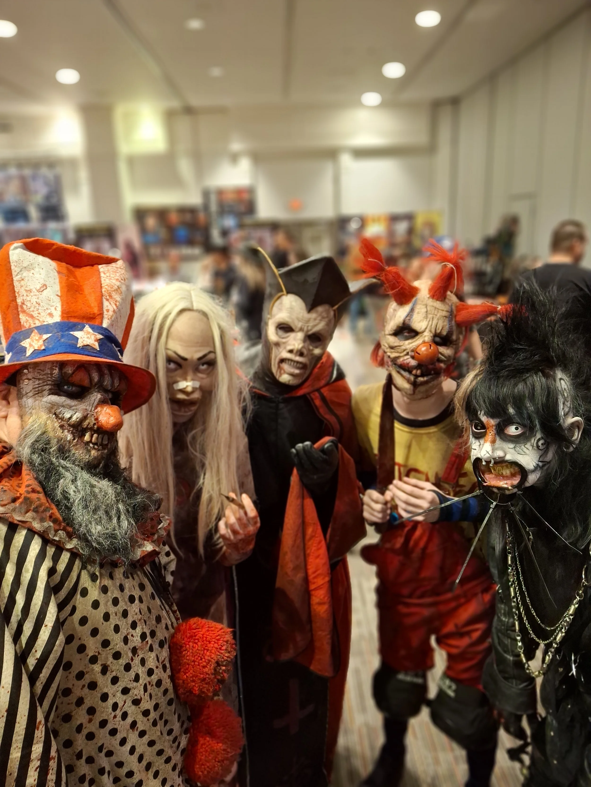 Group of people in Halloween costumes wearing creepy masks at a convention or event.