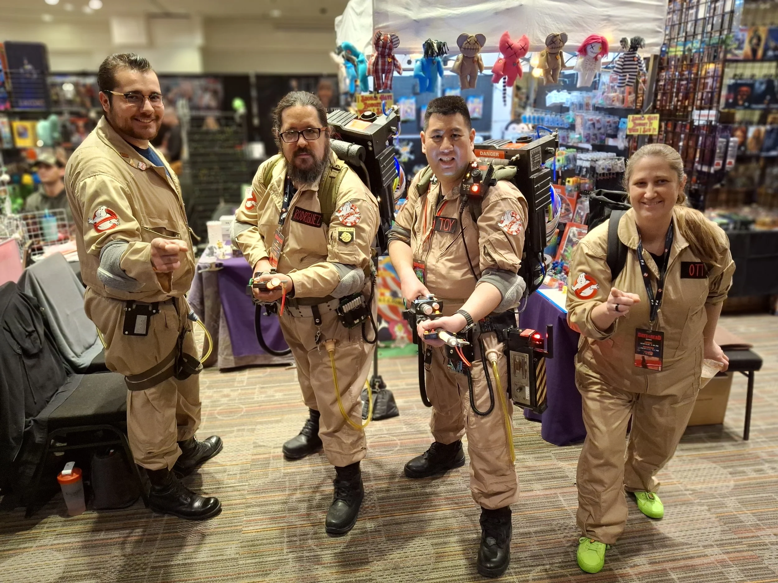 Four people dressed as Ghostbusters in costumes, standing in a store with toys and collectibles in the background.