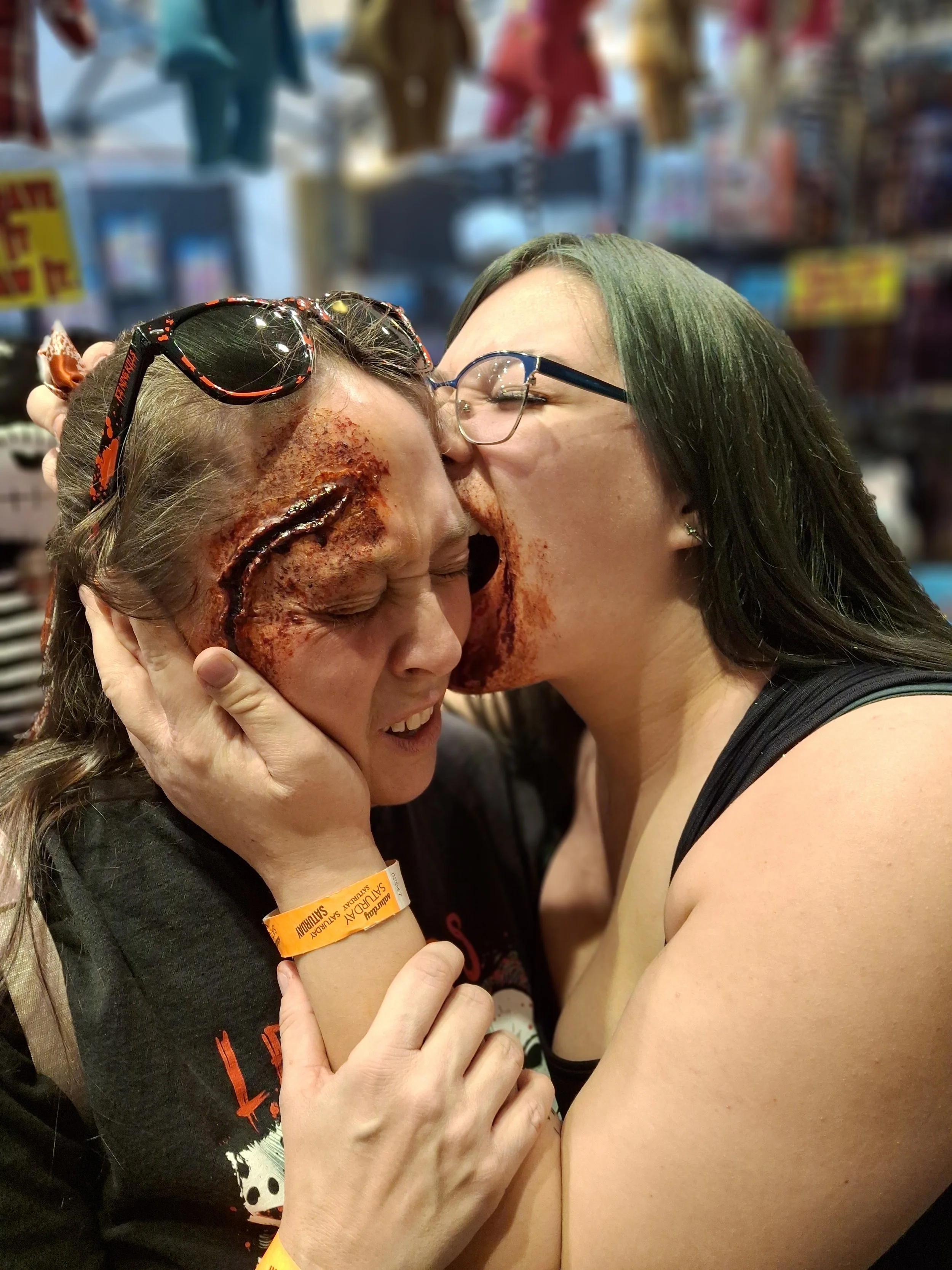 Two women embracing, one with Halloween makeup and the other giving a kiss for Halloween.