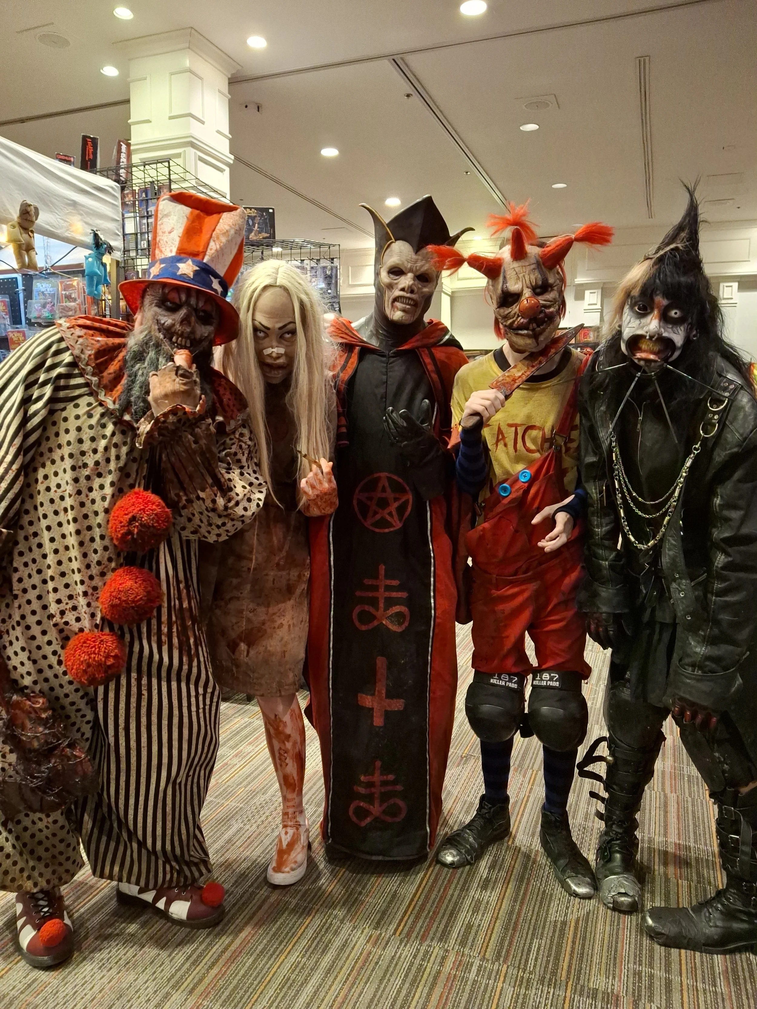 Group of five people dressed in spooky clown and horror movie costumes at a convention.