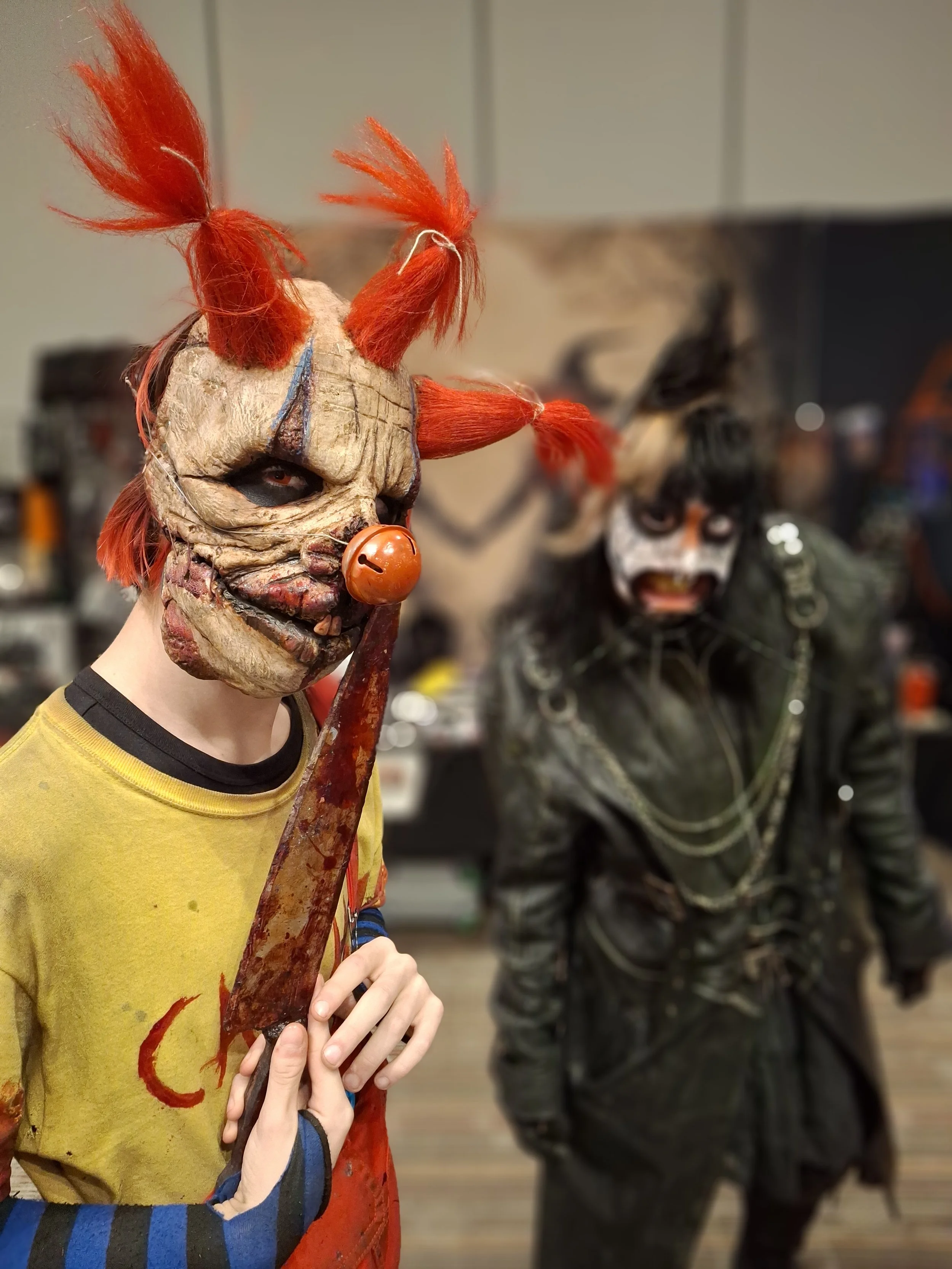 Two people in elaborate horror clown costumes with detailed masks, wigs, and clothing at a costume event.