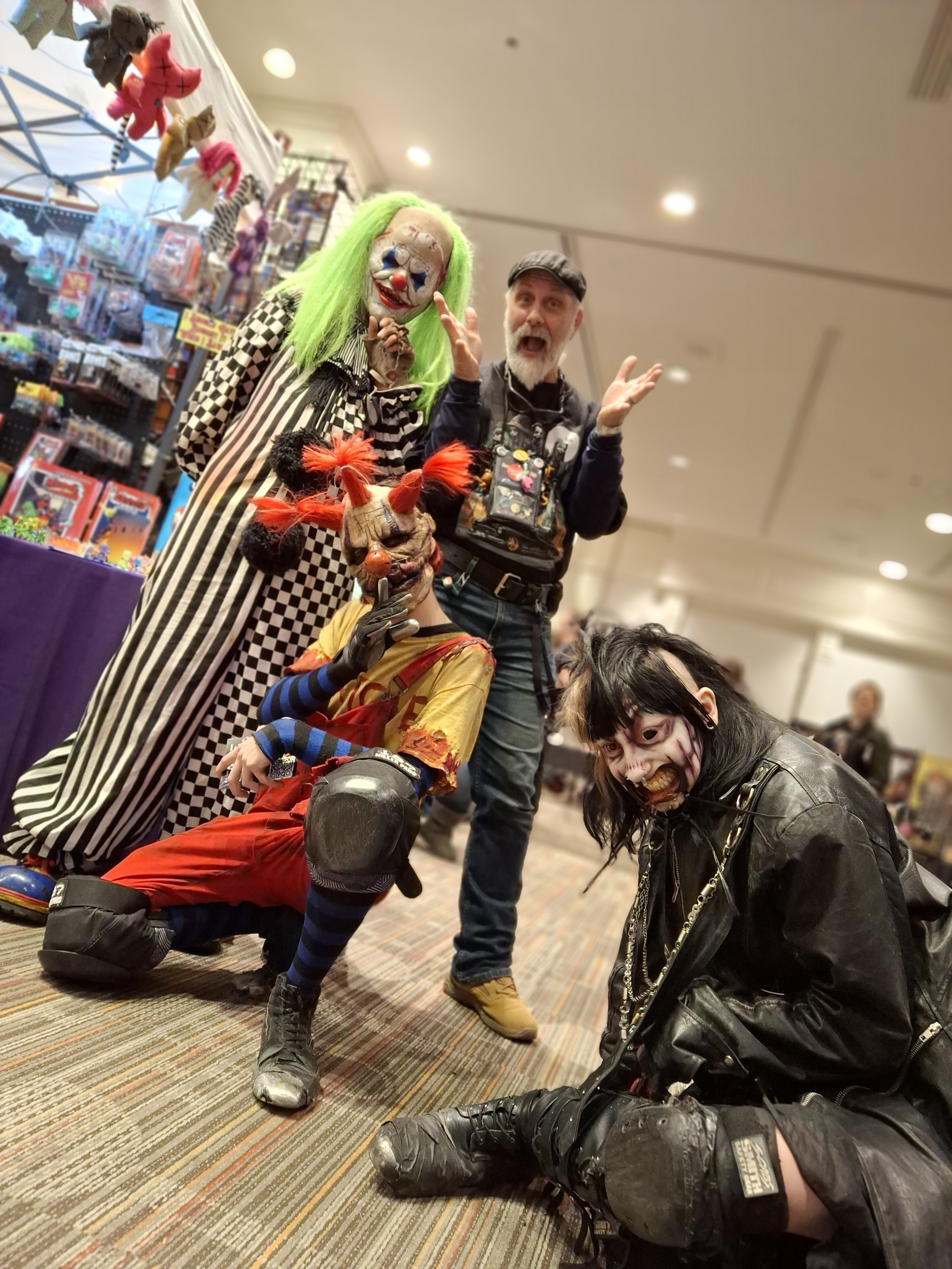 Four people dressed as creepy clowns with scary makeup and costumes, posing indoors at a Halloween or horror-themed event.