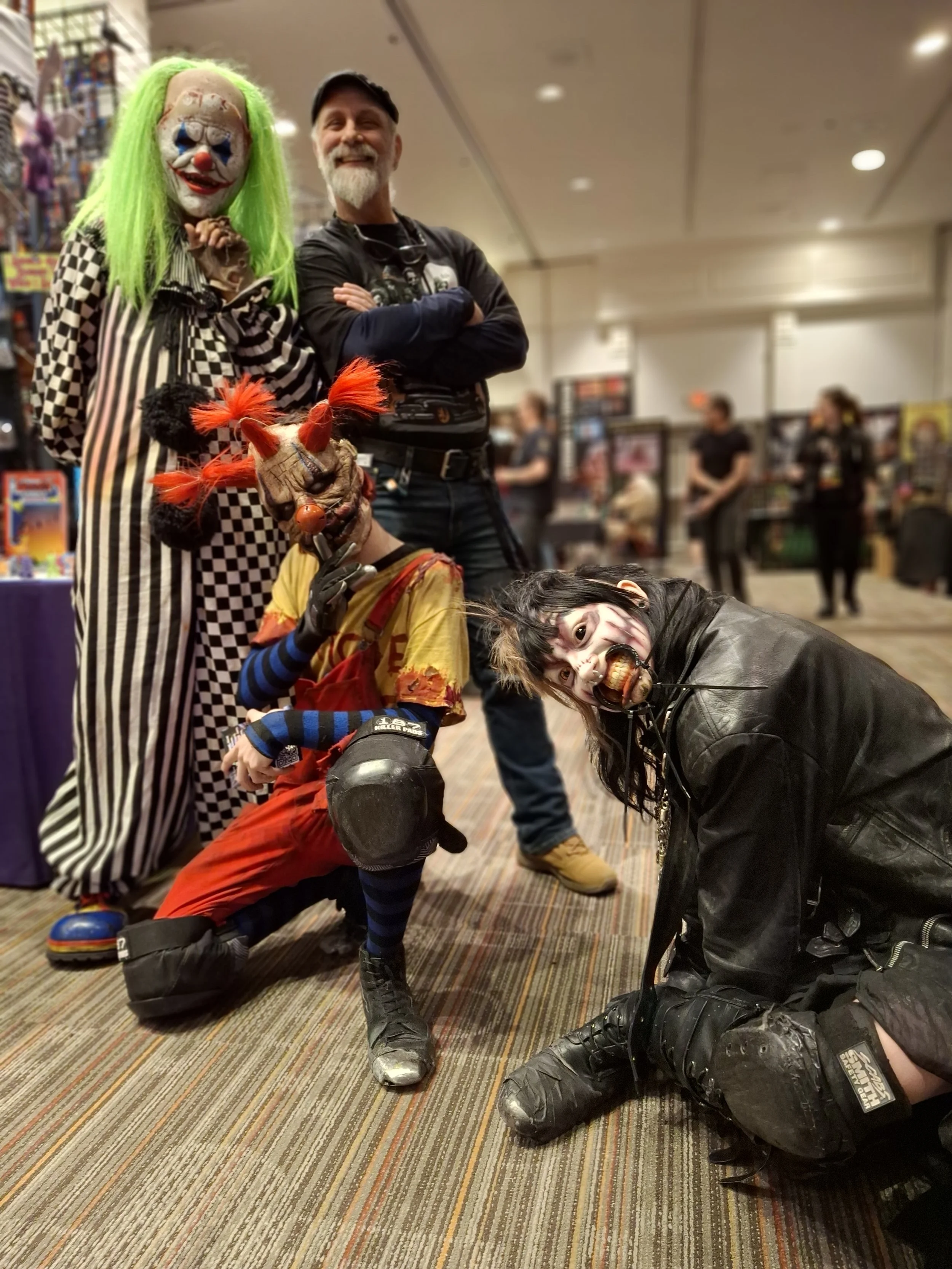 Group of five people in Halloween costumes at a convention, with two adults standing in the back and three children in the front in various creepy costumes.