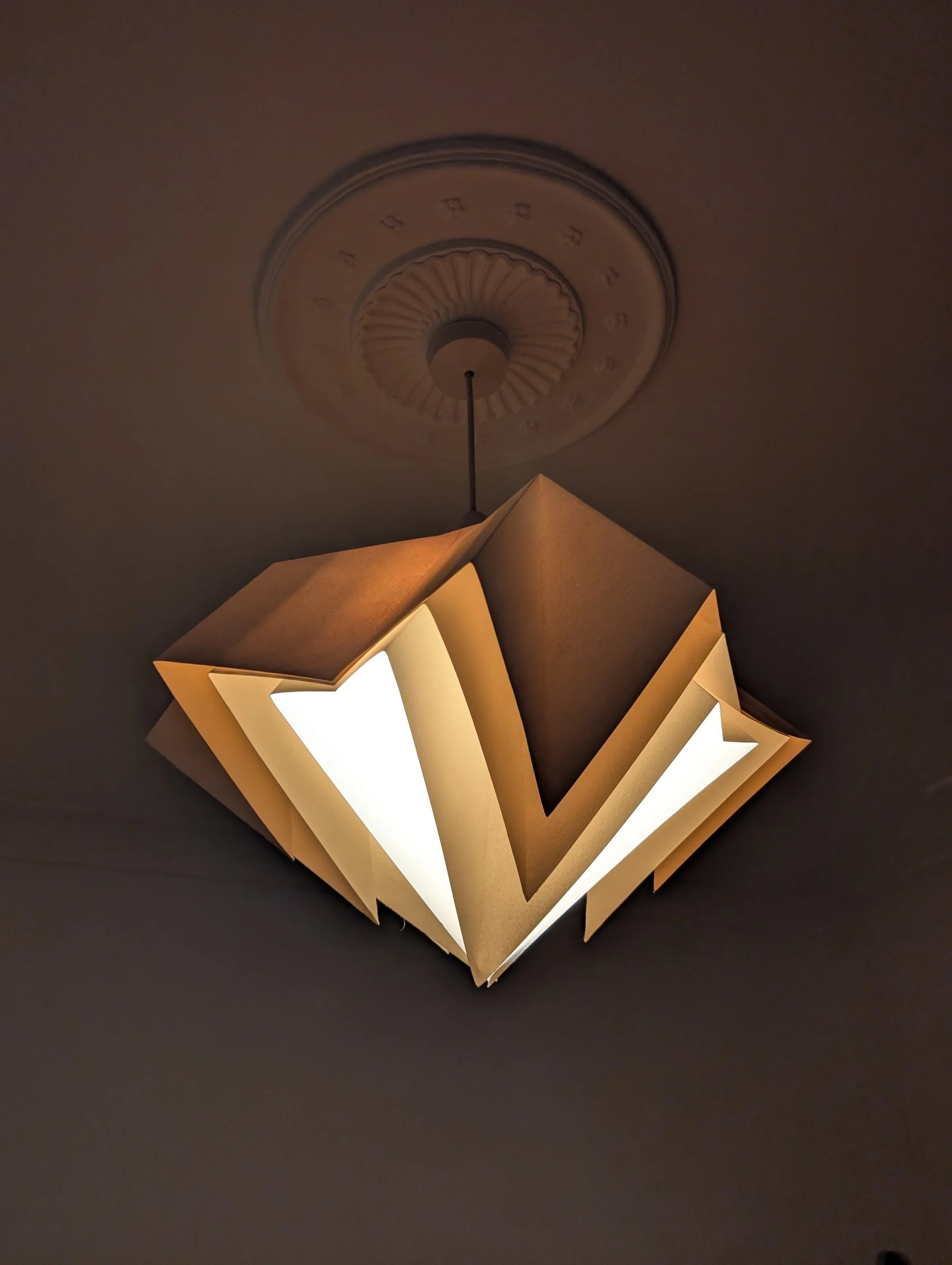 Ceiling light fixture with a geometric design and illuminated panels hanging from a dark ceiling.