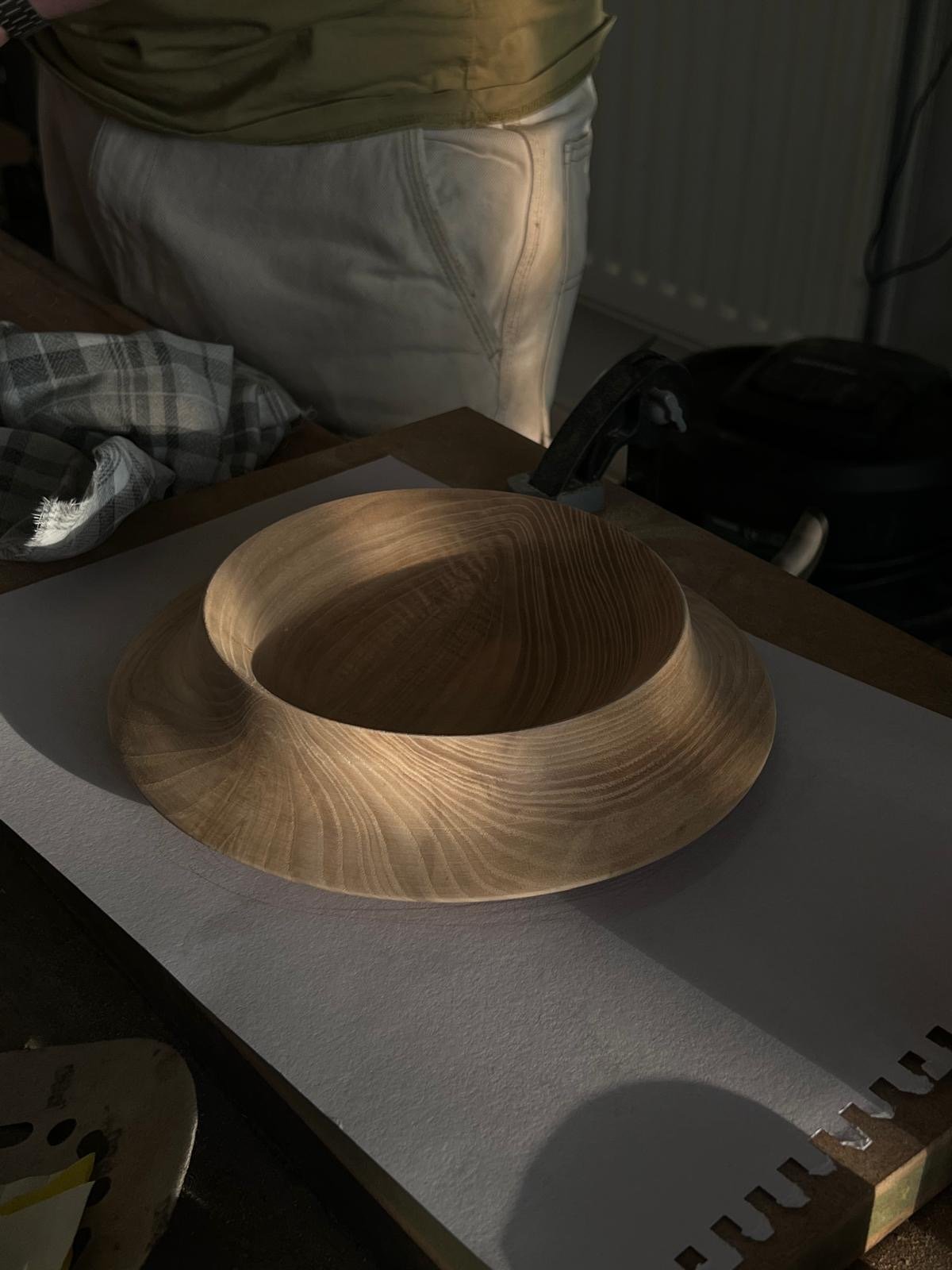 A wooden bowl with a smooth, rounded shape on a table in a dimly lit room.