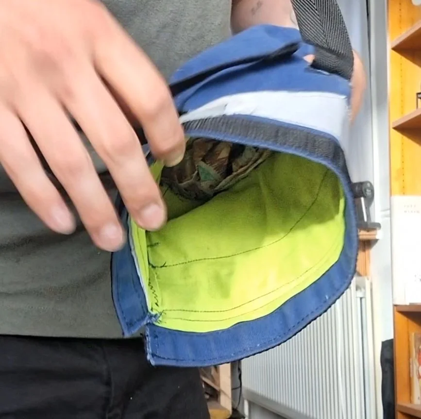 A person is holding open a blue backpack with a neon yellow interior, showing some fabric and items inside.