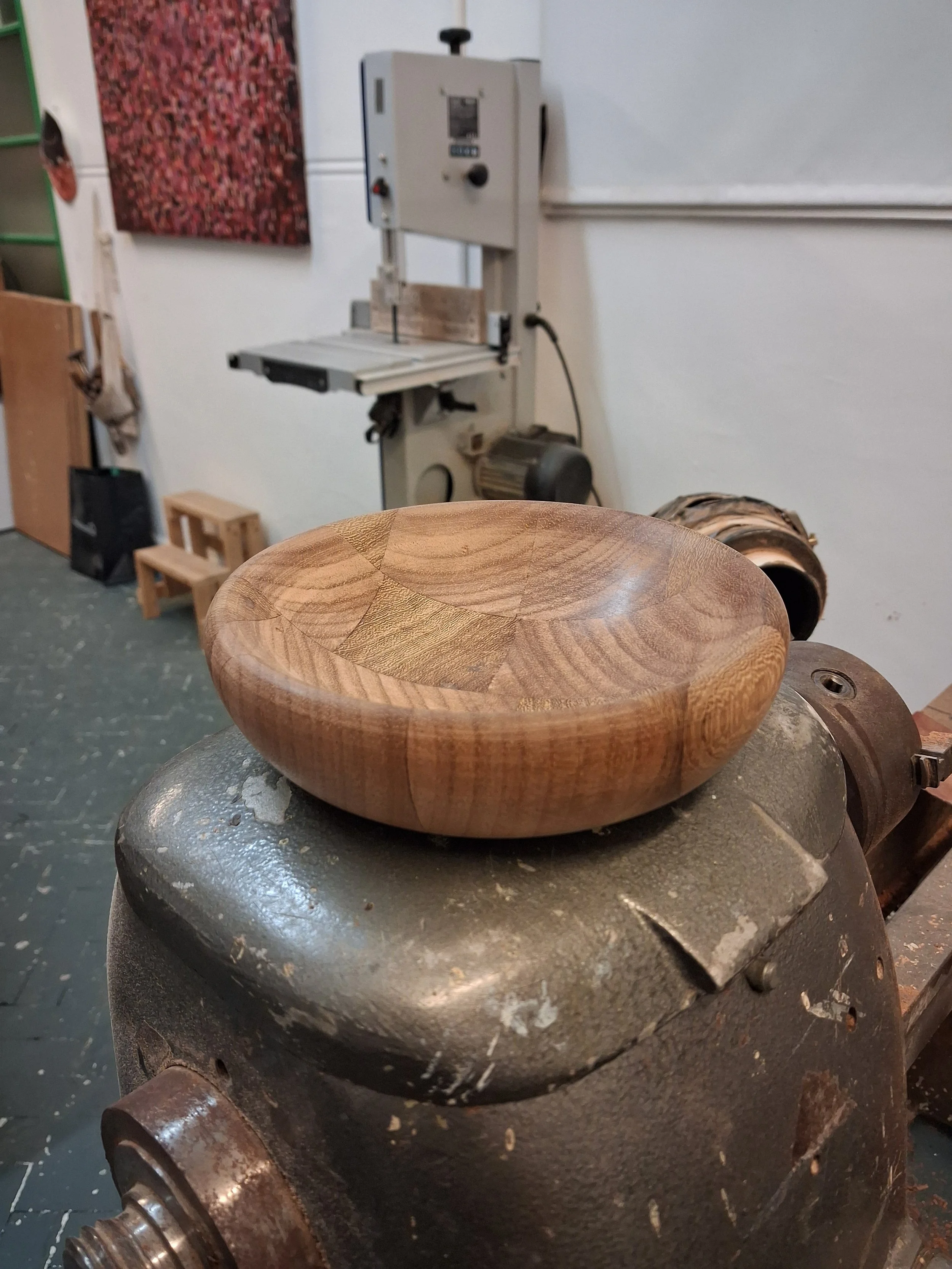 A wooden bowl with a circular pattern on a workbench with woodworking equipment in the background.