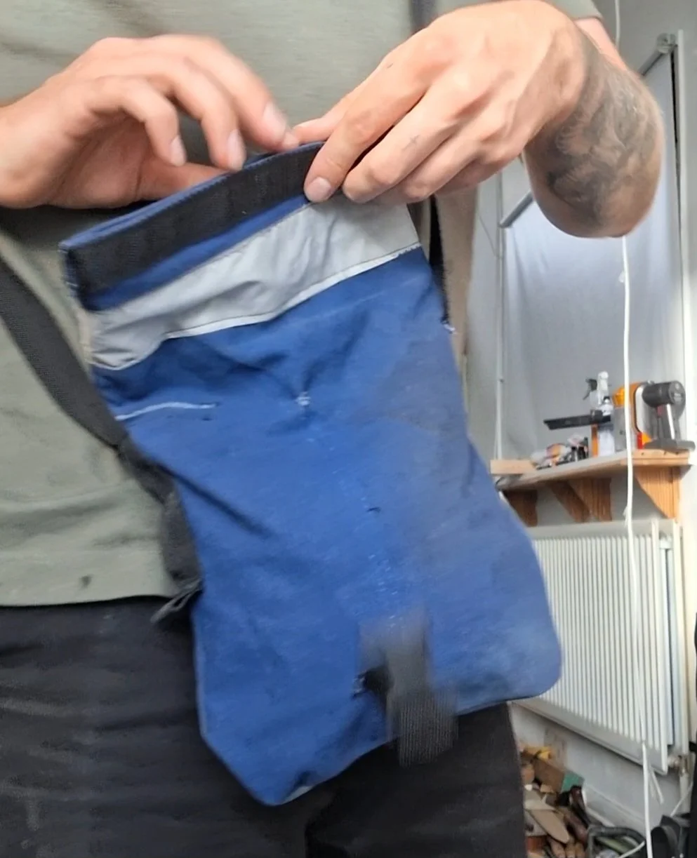 Person opening a blue and gray pouch or bag, showing the inside, in a workshop or garage environment.
