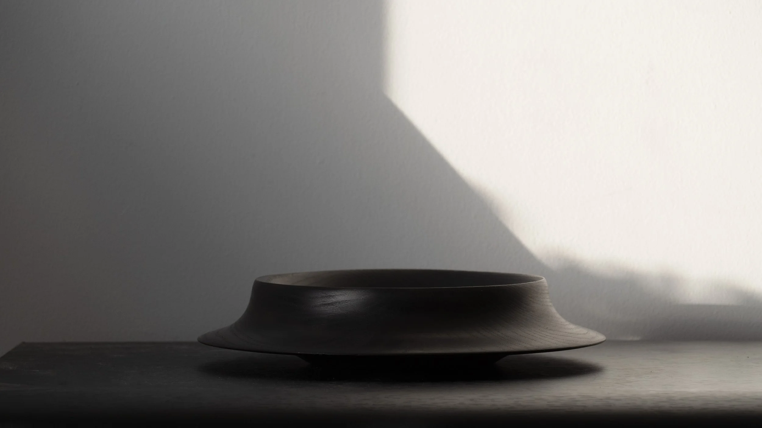 A ceramic bowl on a table with a shadow cast by sunlight on the wall behind it.