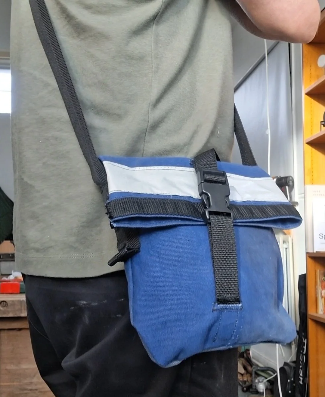 Person wearing a crossbody bag with a rolled-up newspaper inside, in a store or warehouse setting.