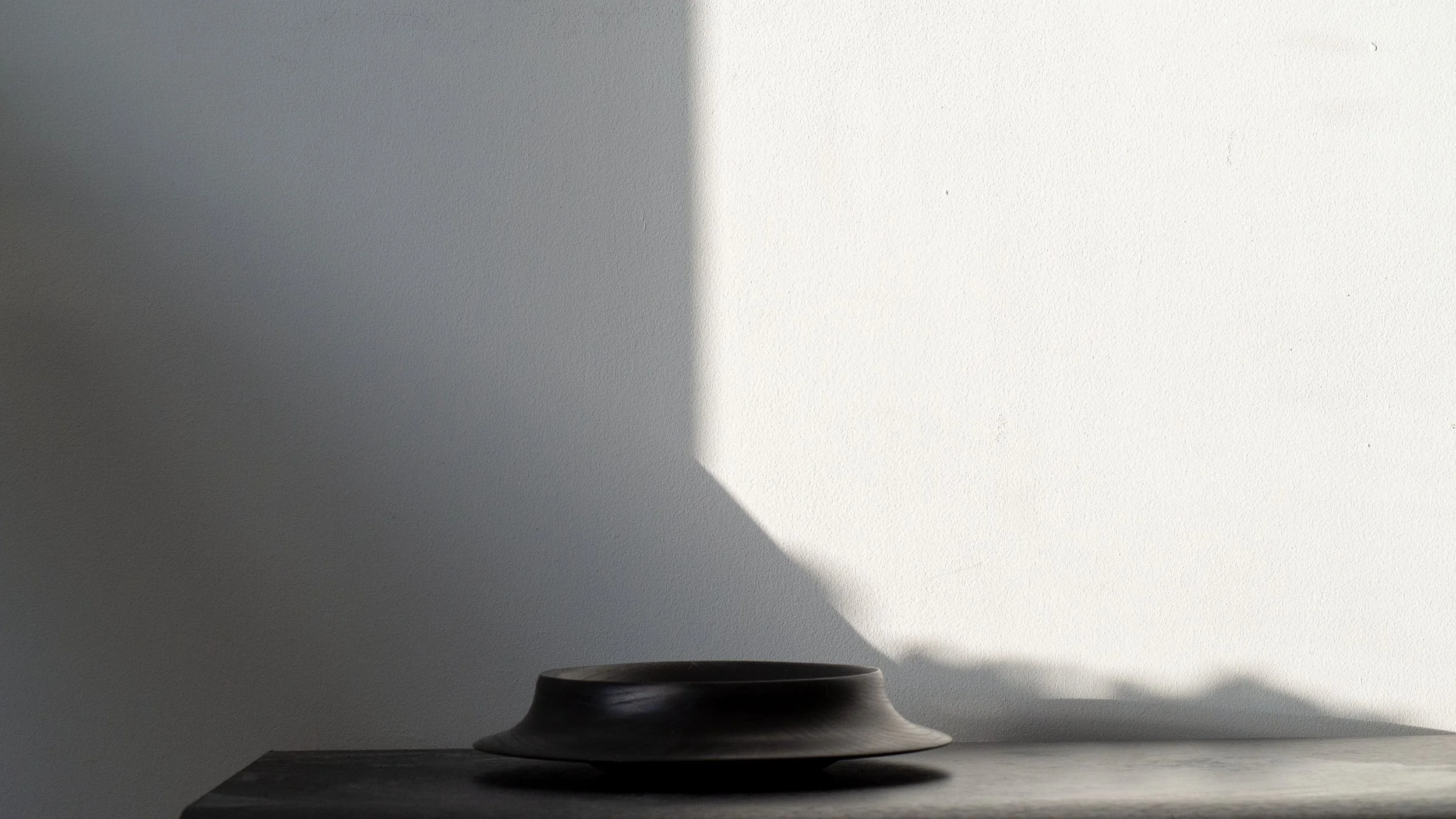 A black object on a gray surface in front of a white wall casting a shadow with a sharp edge.