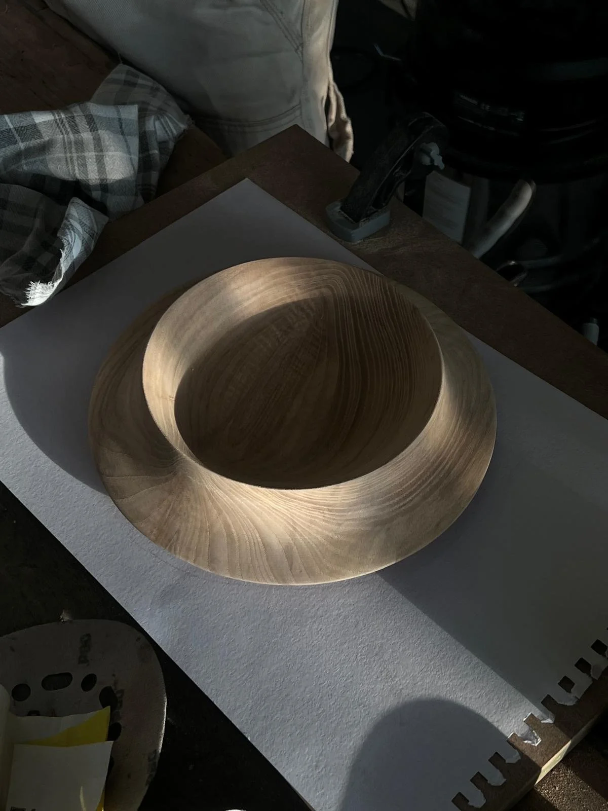 Wooden bowl with a smooth, rounded design placed on a white work surface, surrounded by cloth and workshop tools.