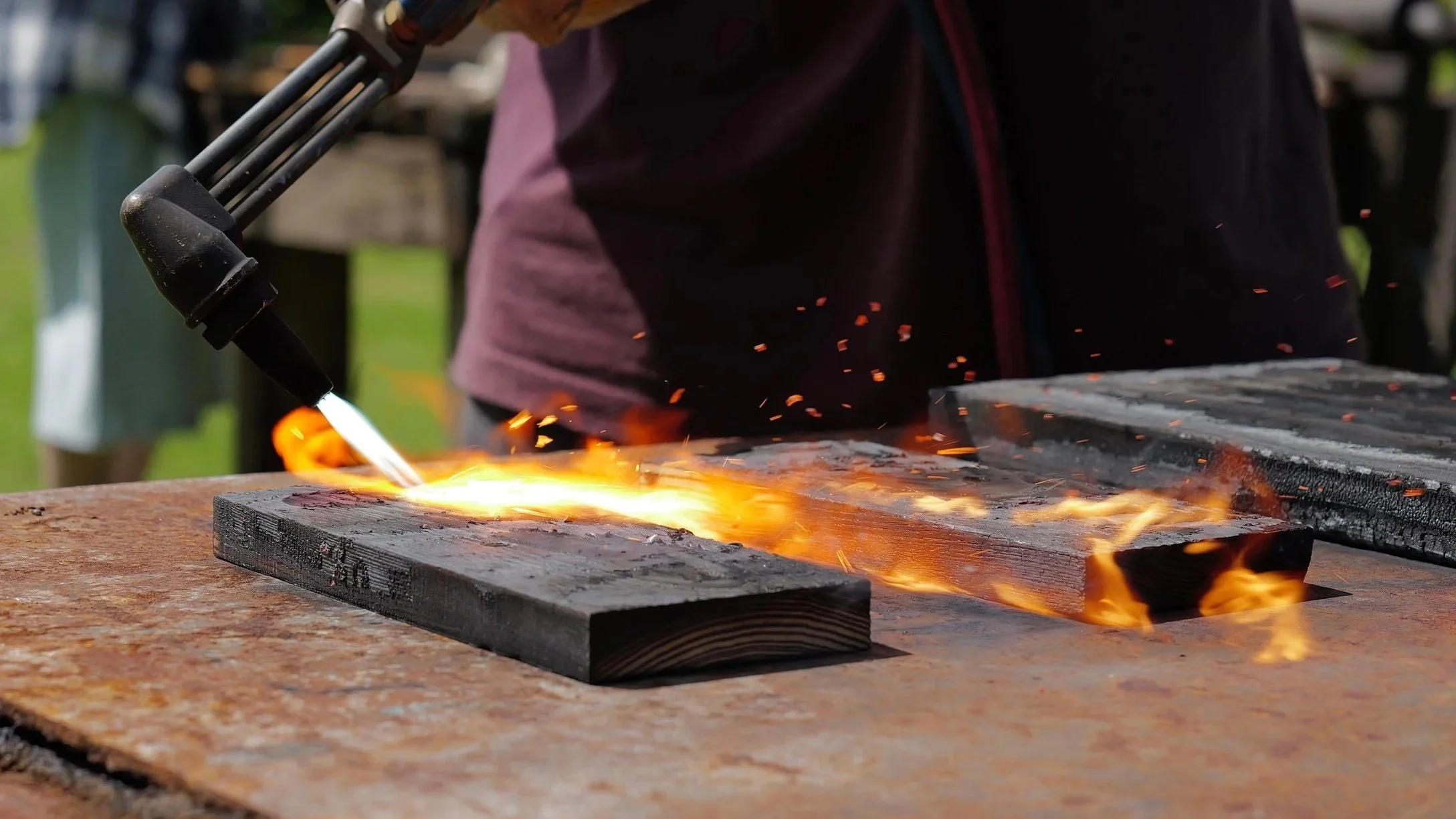 A person welding metal on a wooden workbench, sparks and flames visible as they use a welding torch.
