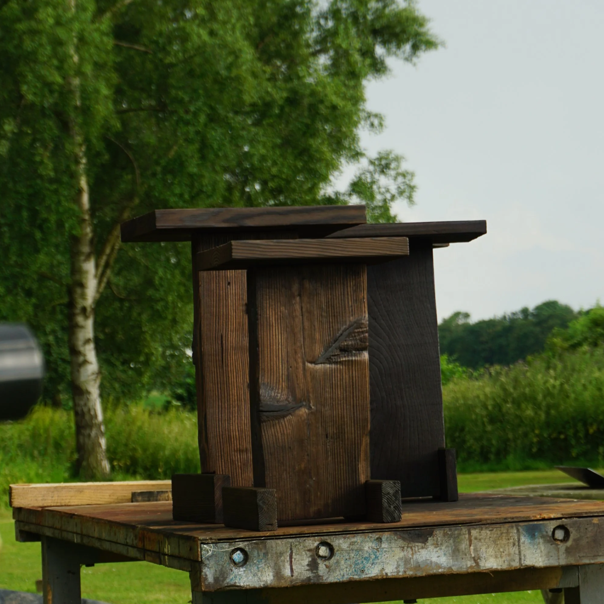 Close-up of a wooden barn swallow birdhouse mounted on a wooden platform outdoors with green trees in the background.