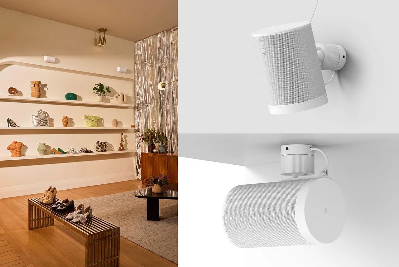 Parte de la sala con estanterías decorativas y zapatos en un banco, y en la otra parte, dos altavoces blancos en la pared.