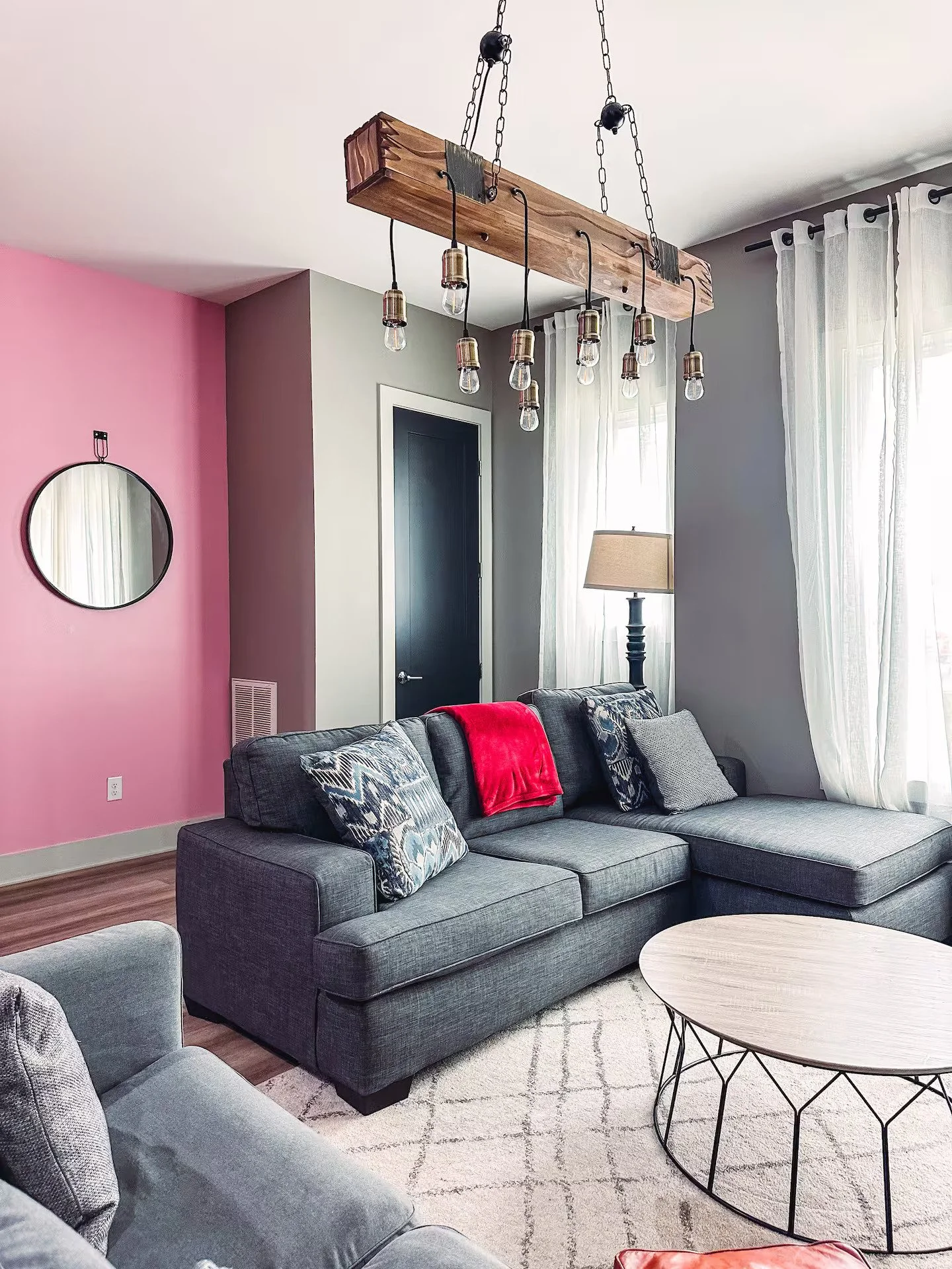 Two grey sofas with a round coffee table, wooden beam light fixture, and grey and pink walls.