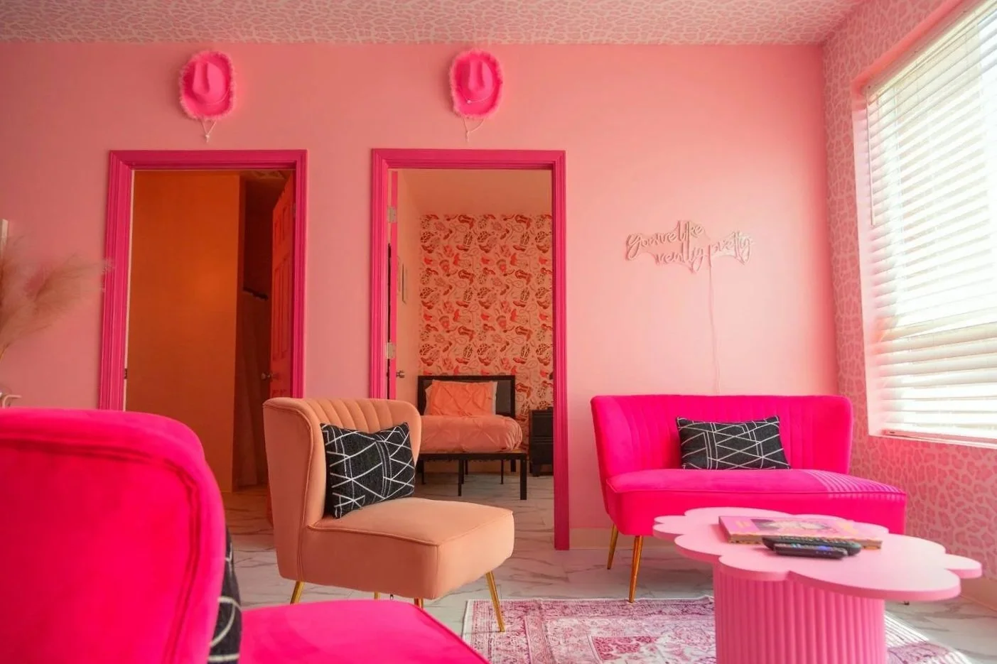 Pretty Inn Pink property sitting area with two accent chairs, a loveseat, and a cloud shaped coffee table in various shades of pink outside of two bedrooms.