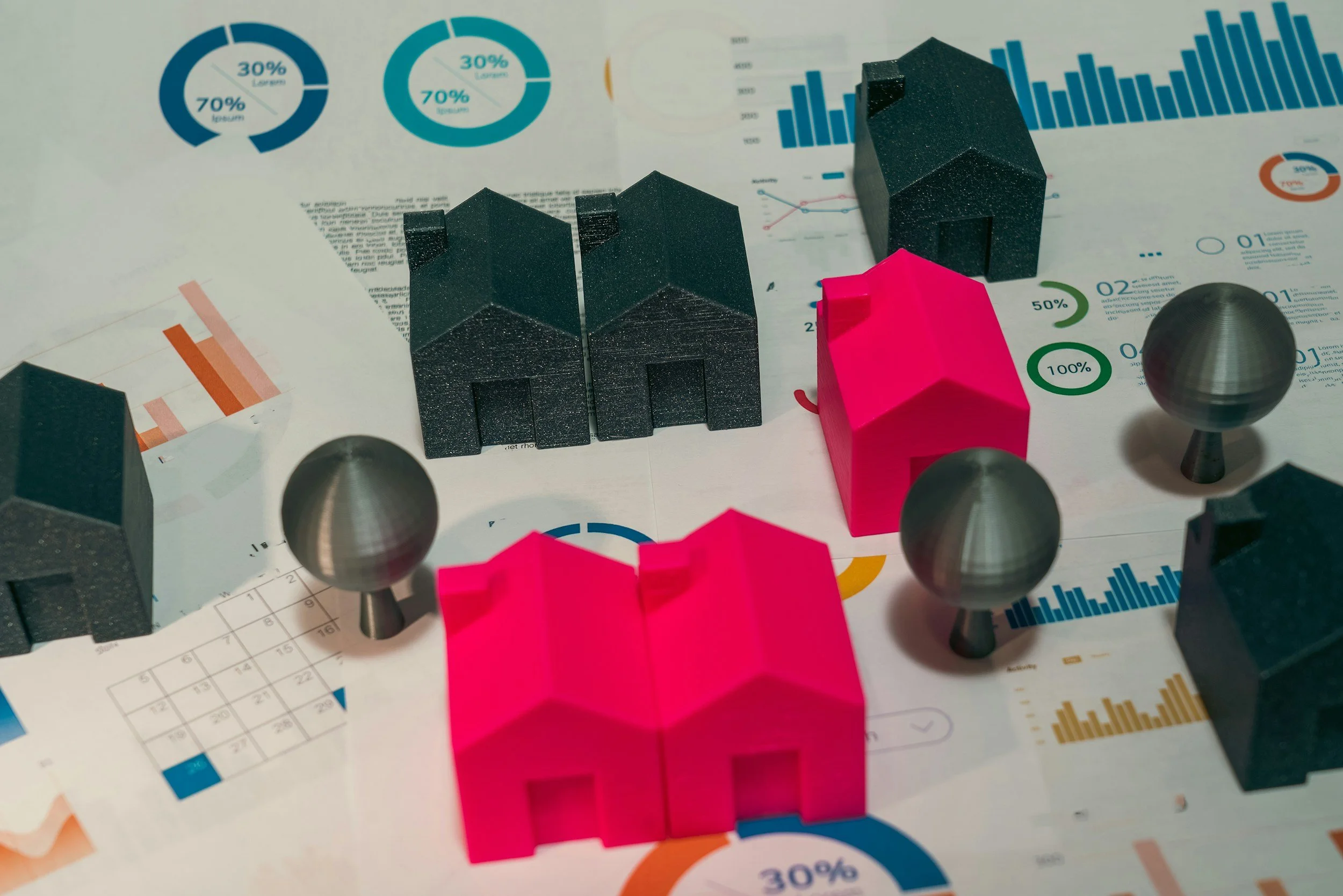 Miniature blank and pink houses sitting on papers of charts to signify property investment.