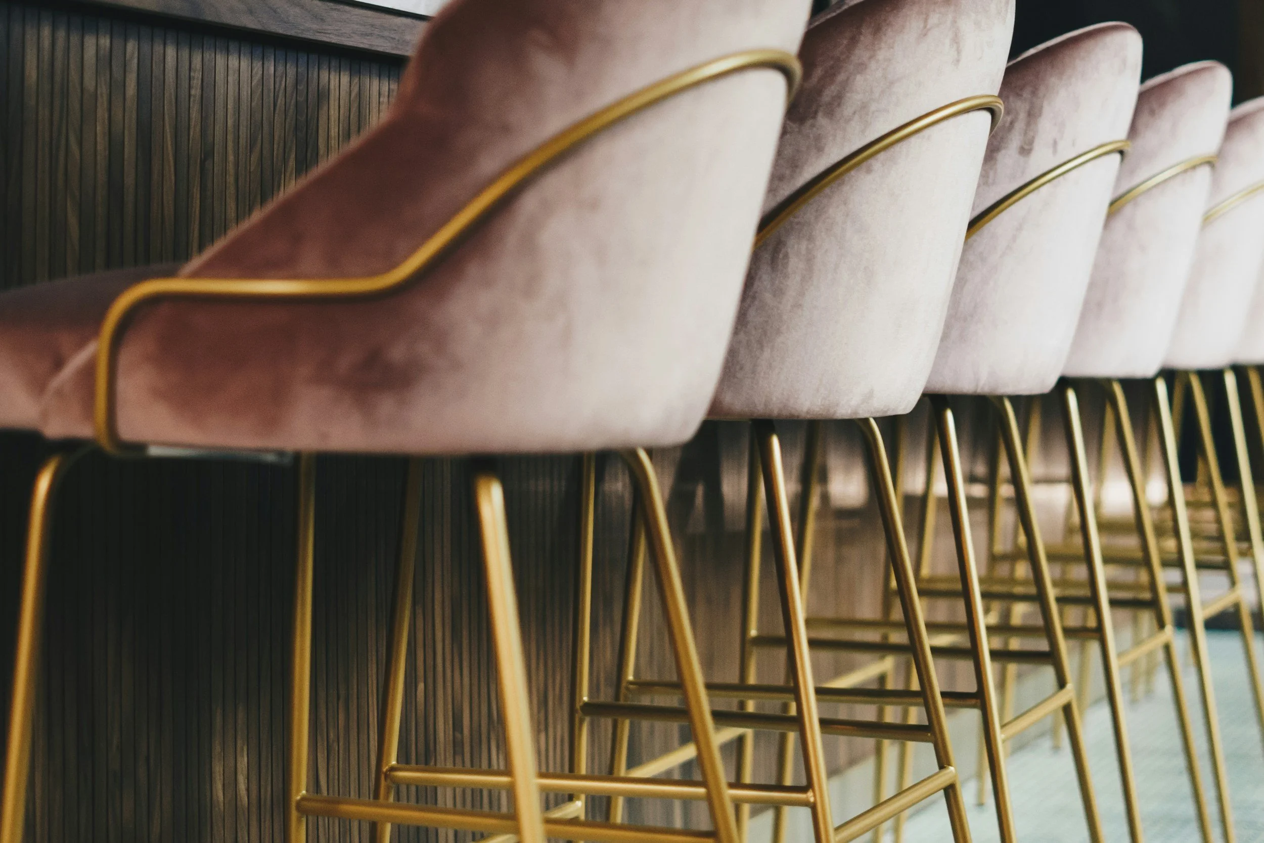 A row of pink velvet barstools with gold legs.