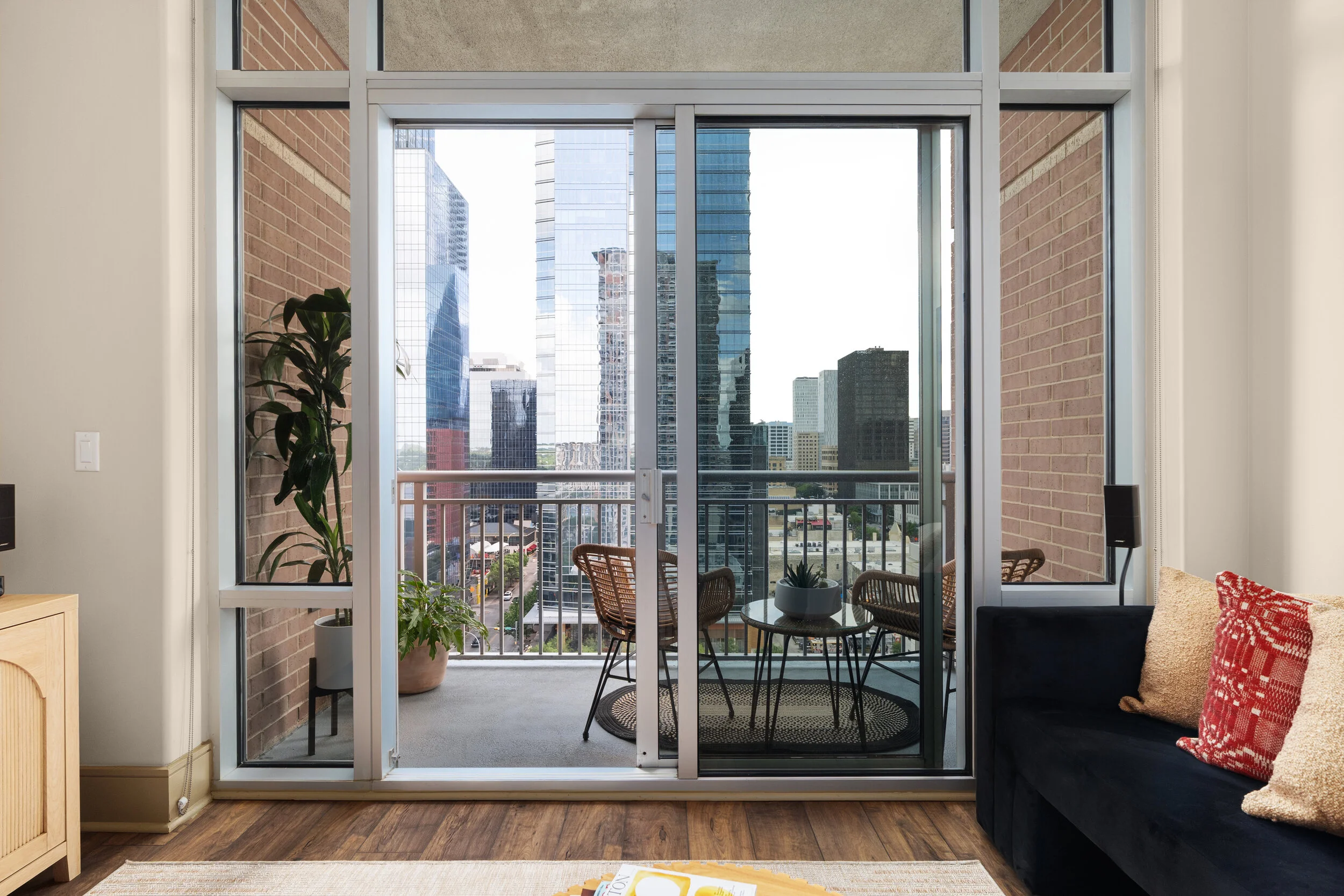 A city loft balcony view, with two floor plants and a small table in between two chairs.