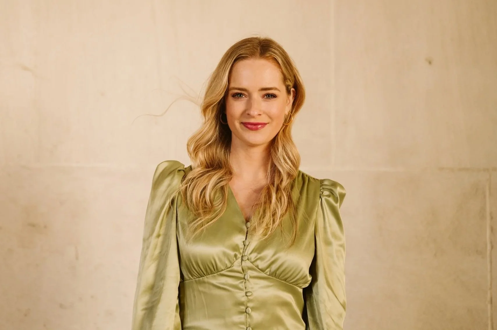 A woman with blonde wavy hair wearing a light green dress with puffed sleeves.