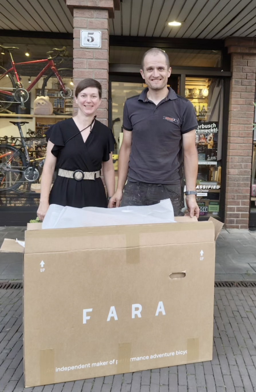 Ein Mann und eine Frau stehen vor einem Fahrradgeschäft und präsentieren ein großes FARA-Produktpaket.
