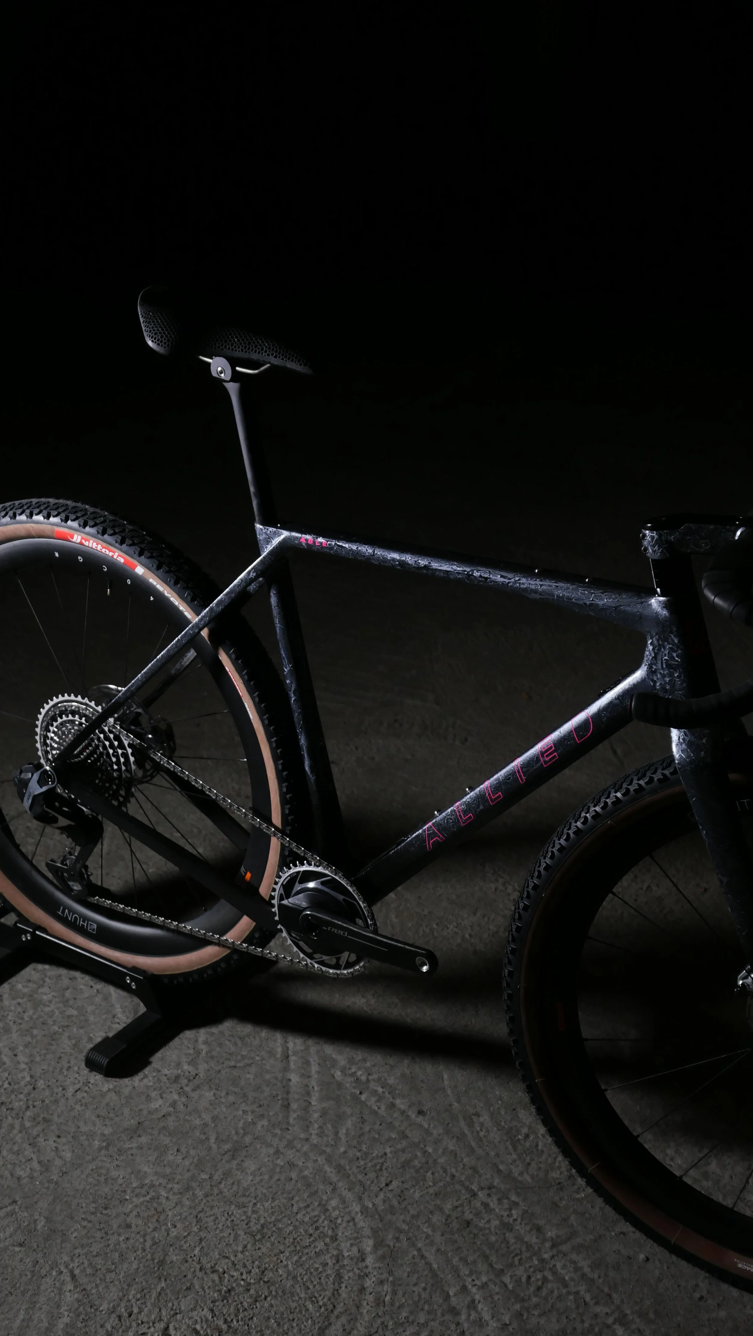 Ein schwarzes Mountainbike mit beige Reifen auf einem dunklen Boden bei Nacht.