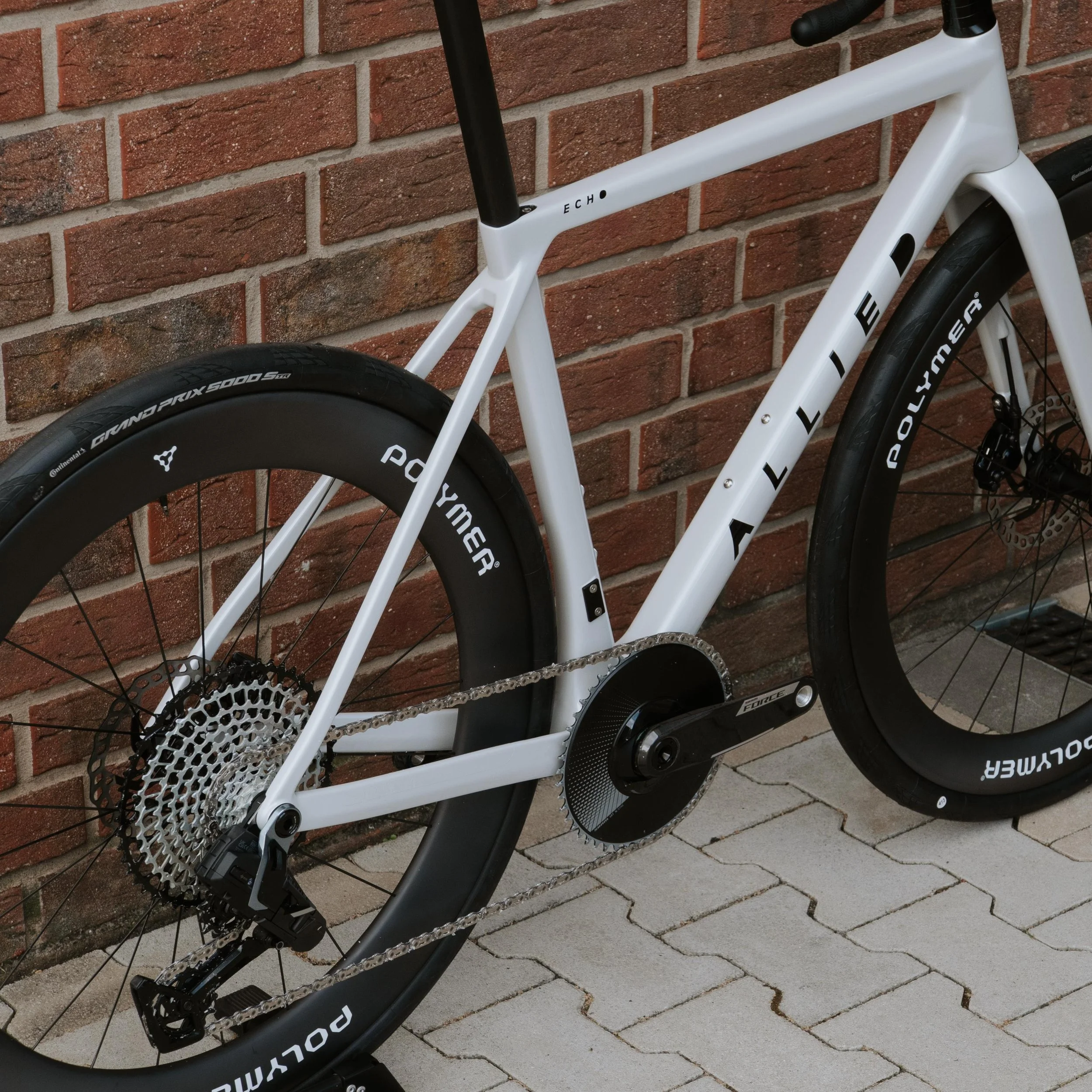 Ein weißes Rennrad mit schwarzen Reifen, das an einer roten Backsteinmauer steht.