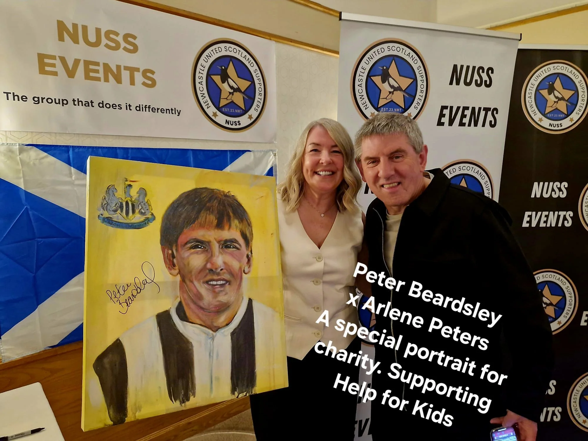 A man and a woman smiling and posing for a photo at an event supporting charity for kids, with a colorful portrait of a young man in a jacket and signature visible in front of them. The background includes banners for Newcastle Scotland Supporters Society (NUSS) Events.