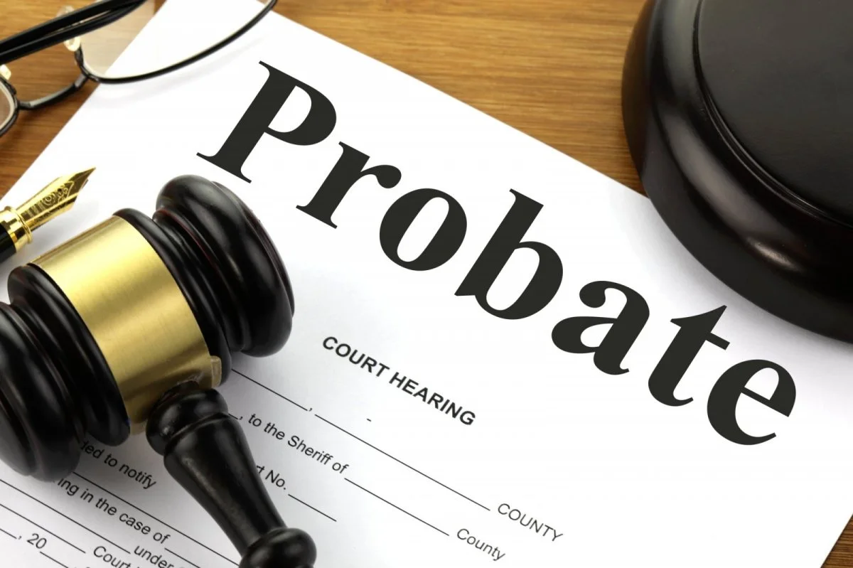 A legal document titled Probate lies on a desk next to a wooden gavel, a pair of glasses, and part of a judge’s block, symbolizing a court hearing regarding a probate case.