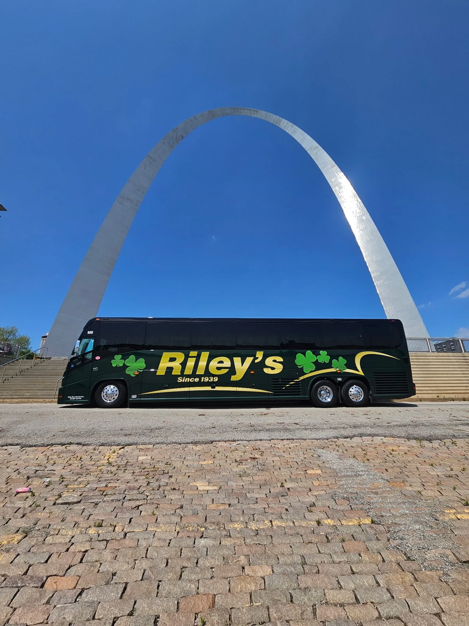 A black bus with green shamrocks and yellow text that reads "Riley's Since 1939" parked in front of the Gateway Arch in St. Louis, Missouri.