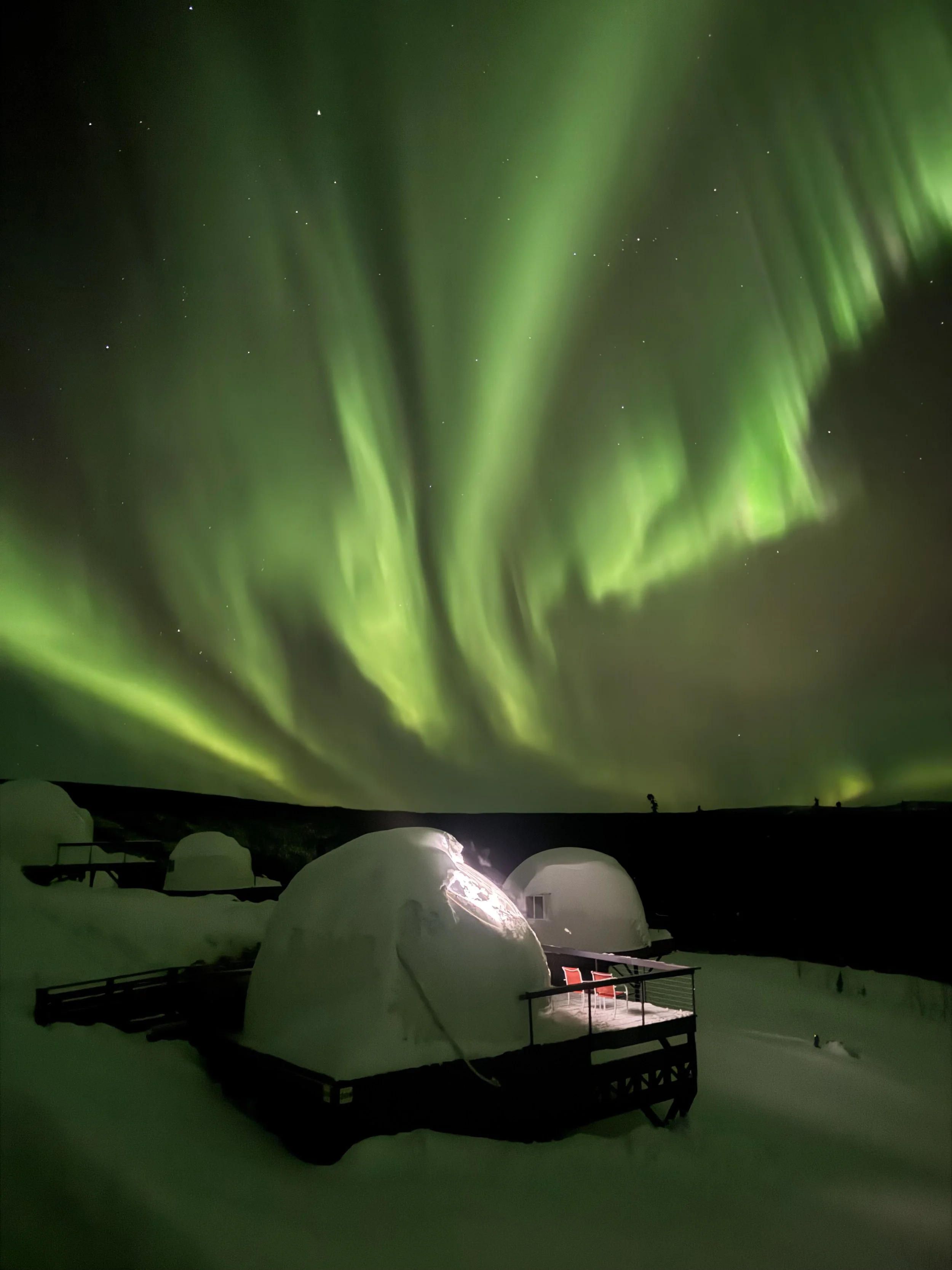 Northern lights over a mountain landscape with trees and a river reflecting the sky