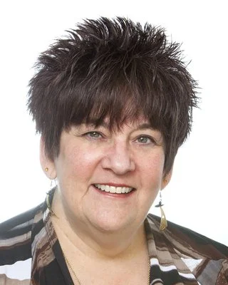 A smiling woman with short, spiky dark hair and wearing earrings, against a plain white background.