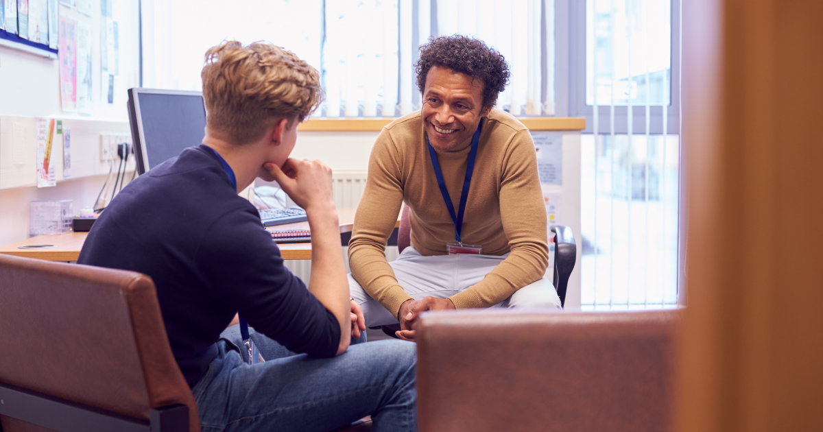 A young man and an older man having a conversation in an office setting, both smiling.