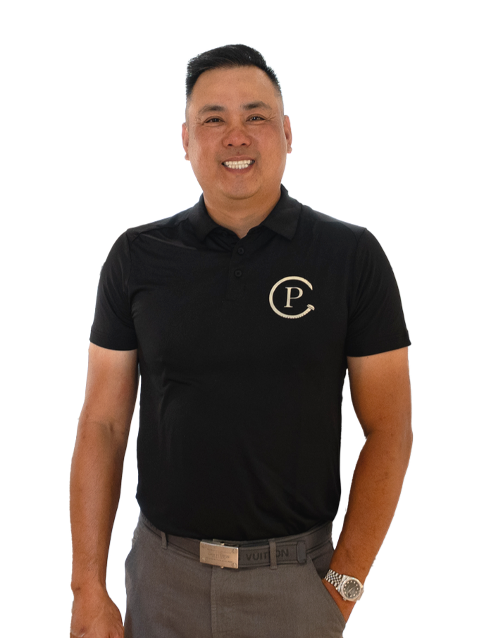 A man smiling, wearing a black polo shirt with a 'P' logo, gray pants, and a watch, standing against a black background.