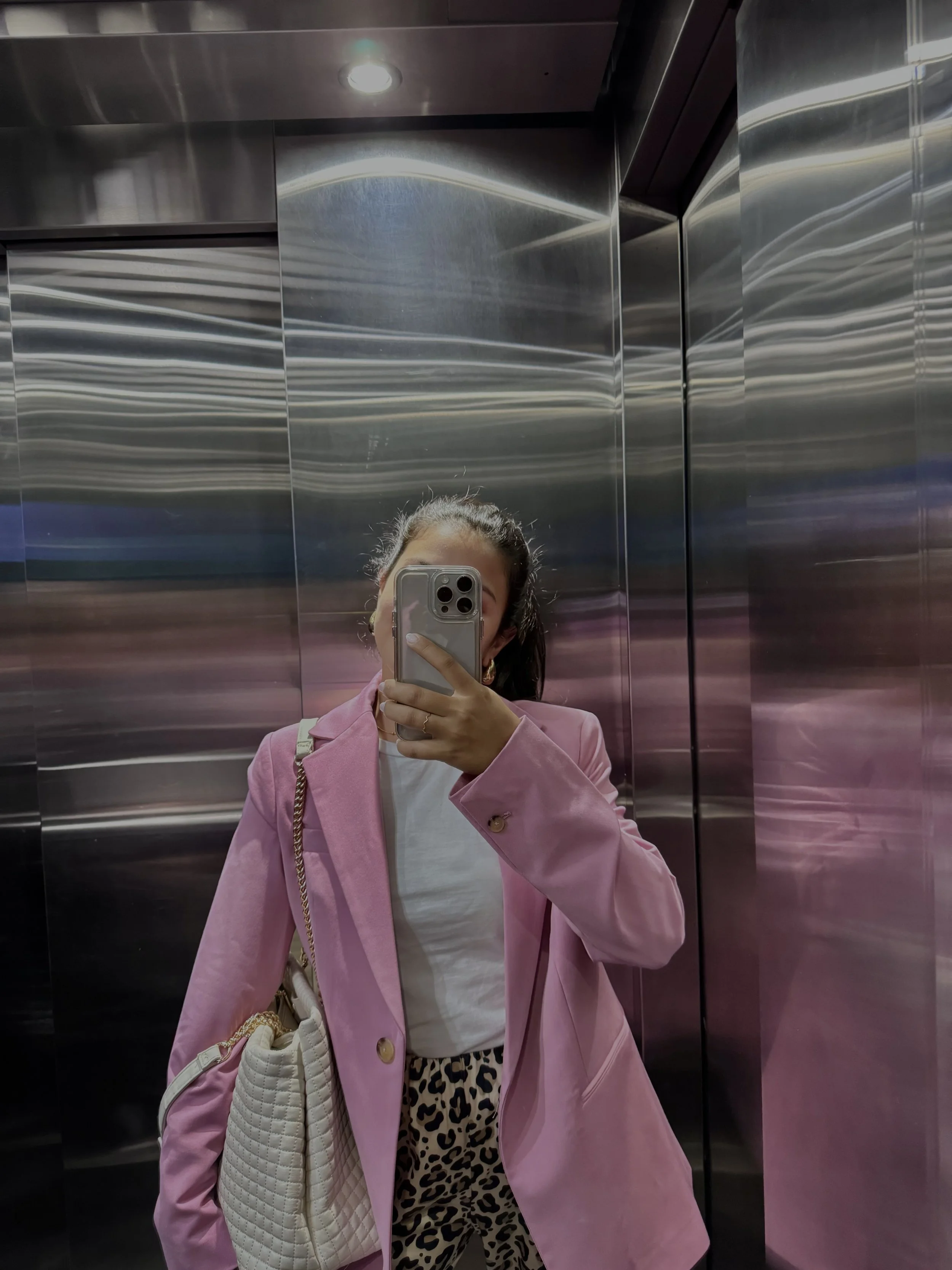 Mirror selfie in an elevator wearing a pink blazer over a white tee with leopard print pants and a white quilted shoulder bag