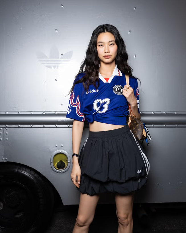 Actress Hoyeon at an Adidas event wearing a South Korea soccer jersey, black bubble Adidas mini skirt, and a Louis Vuitton handbag over her shoulder.