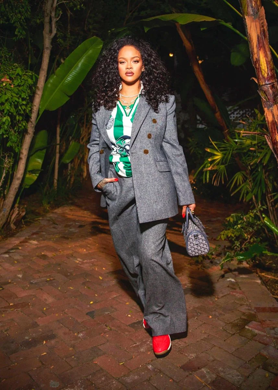 Artist Rihanna wearing a striped green and white soccer jersey with a tailored greem suit, red sneakers, and a handbag.