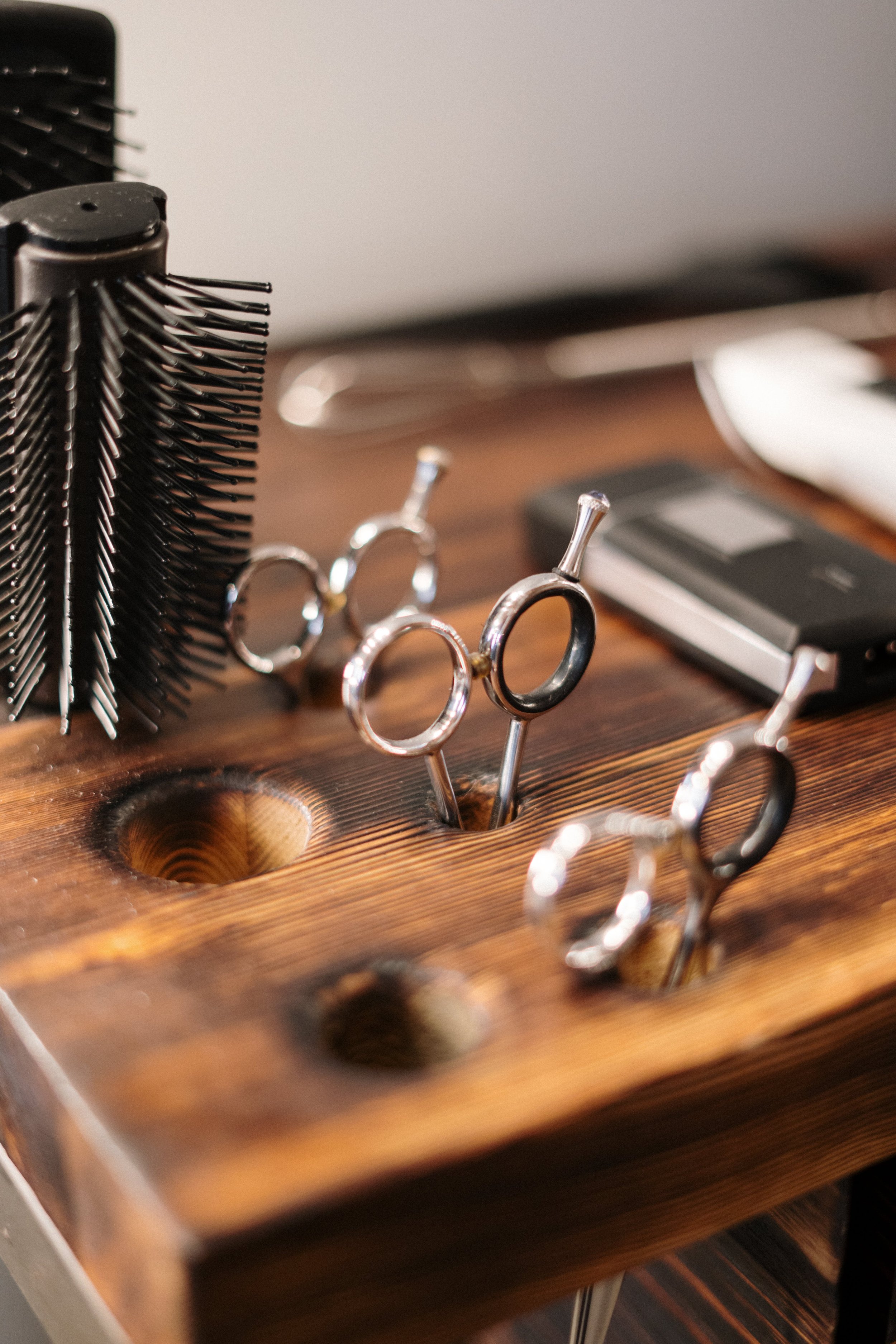 Close-up of a wooden hairstyling tool stand with scalp scissors, hair clips, and a hairdryer on a wooden surface.