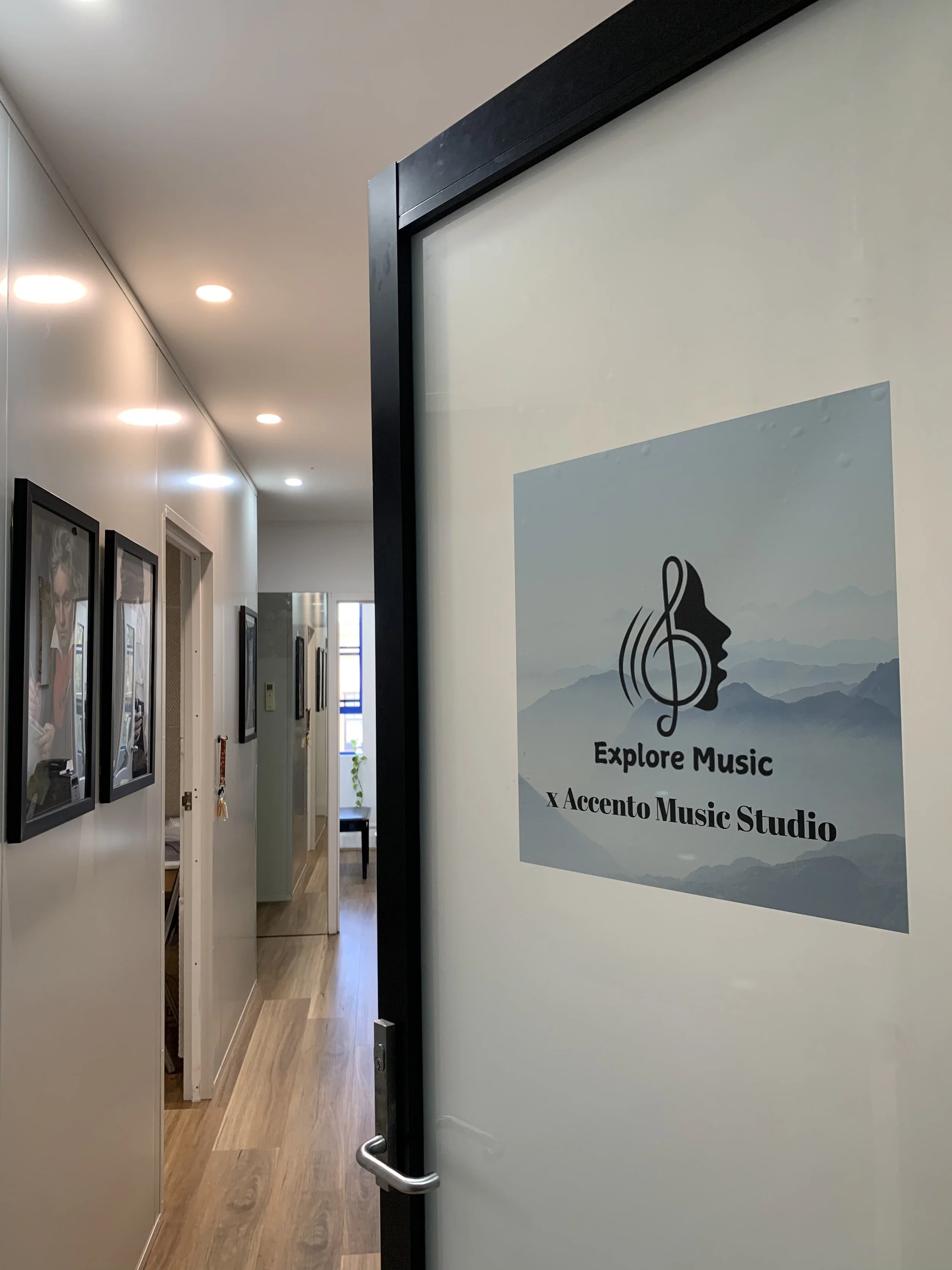 A hallway inside a music studio with framed photos on the wall and a sign that reads 'Explore Music, X Accento Music Studio'.