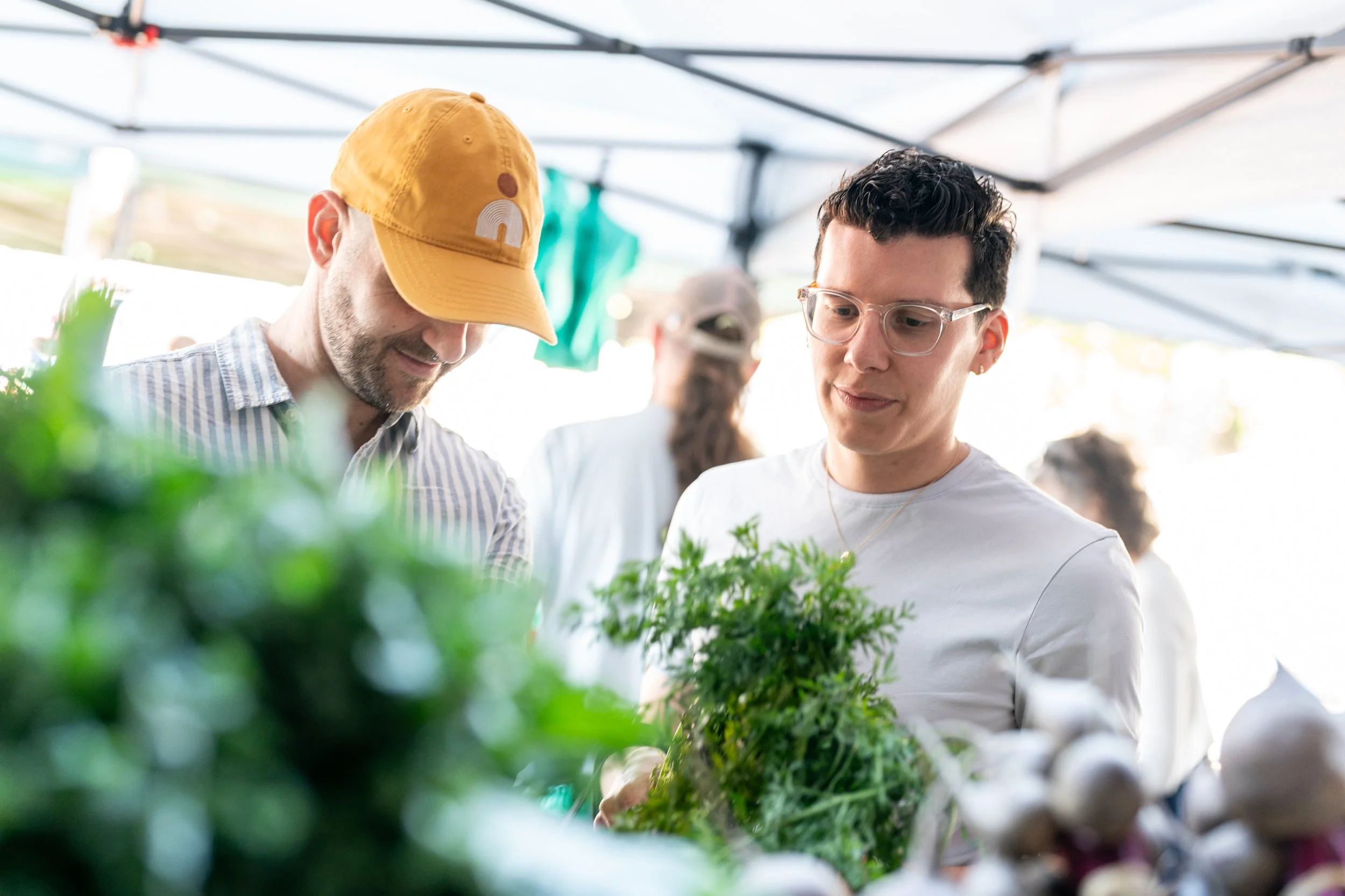 Two people, including Adrian, purchasing  produce at a farmers market.