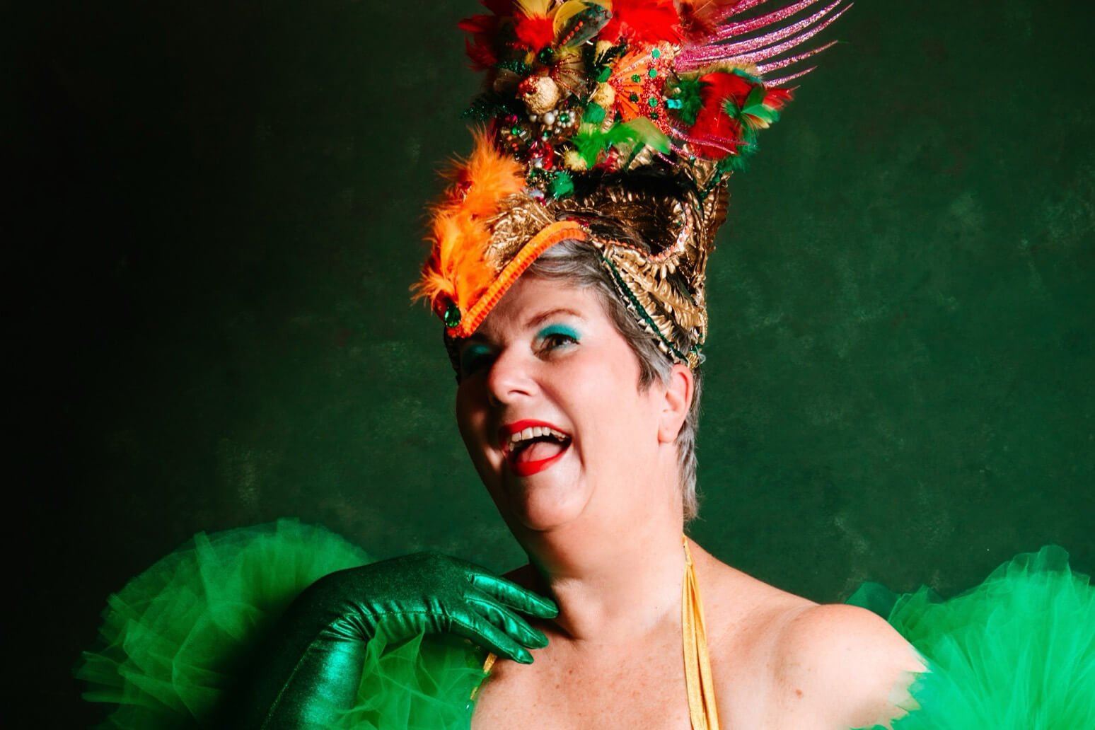 A white person in makeup and a big fancy hat wearing green gloves and a green dress