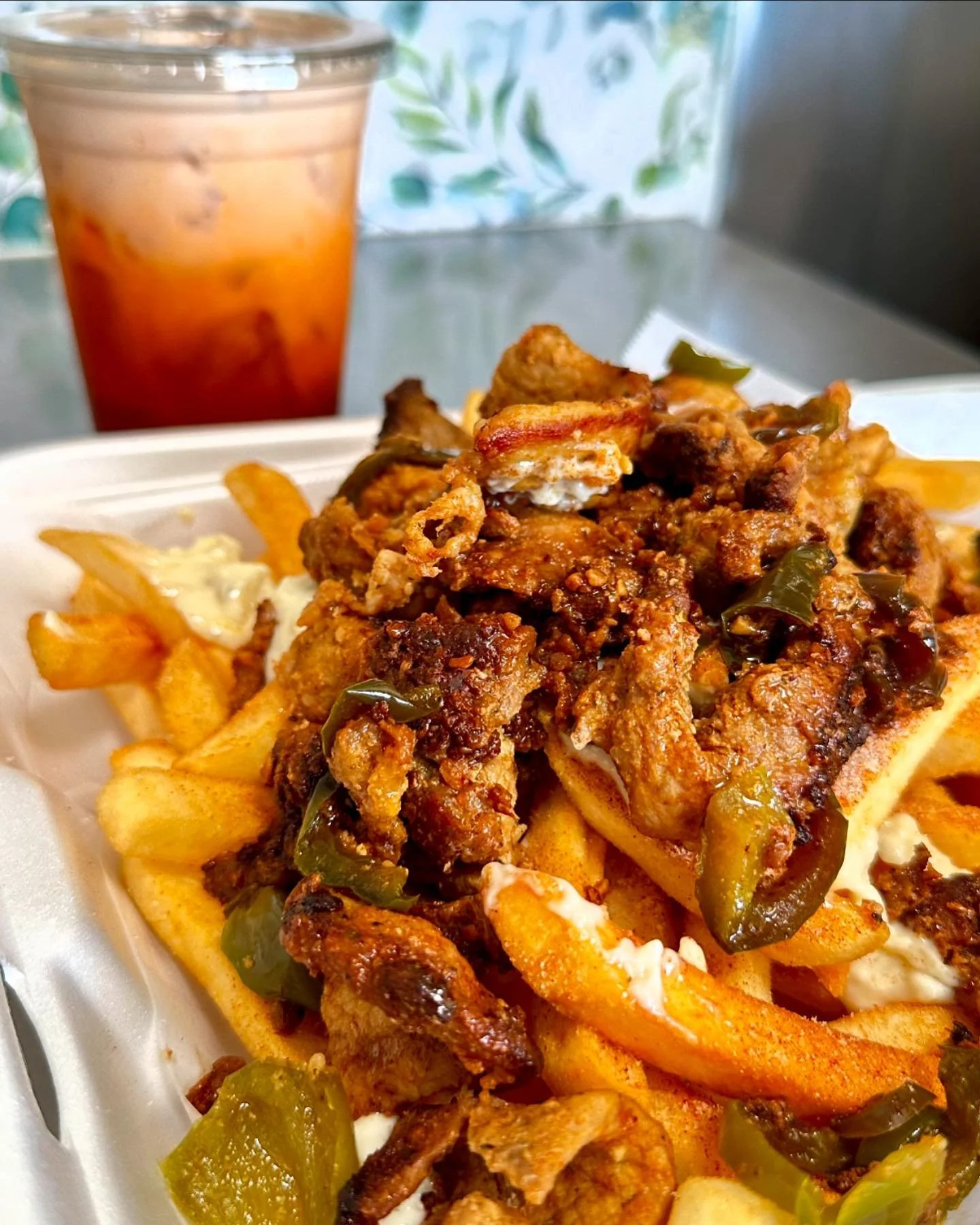 Fried chicken and fries with green peppers on a foam tray, with a drink in the background.