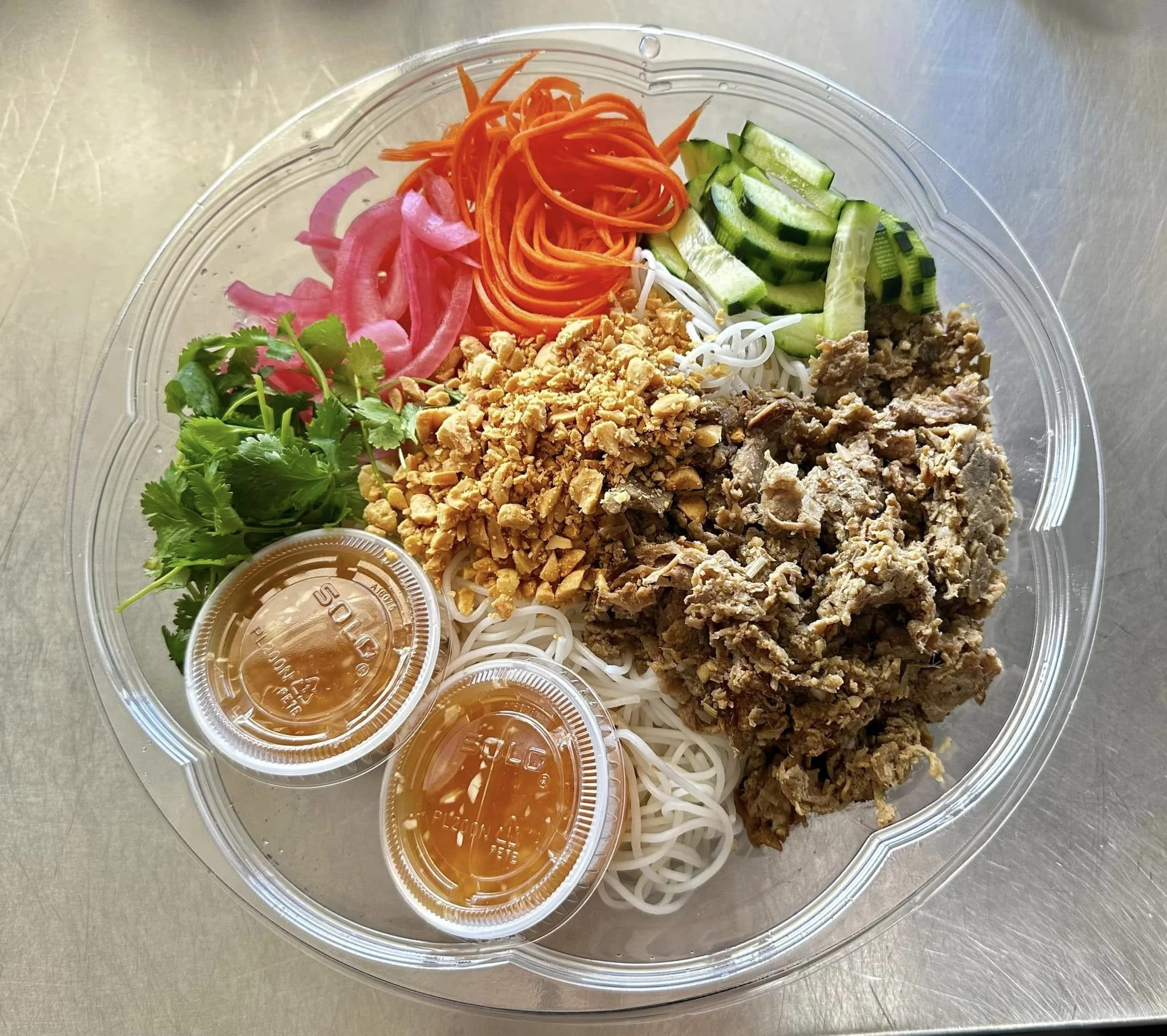 Container of prepared Asian noodle salad with vegetables, crushed peanuts, and two small containers of sauce.