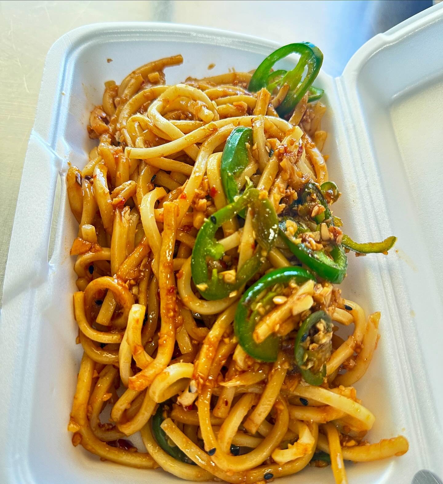 Stir-fried noodles with green bell peppers and chopped vegetables in a takeout container.