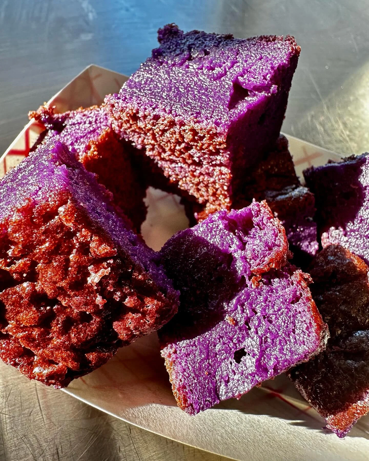 Close-up of purple-colored, baked sweet potato cubes on a white paper tray.